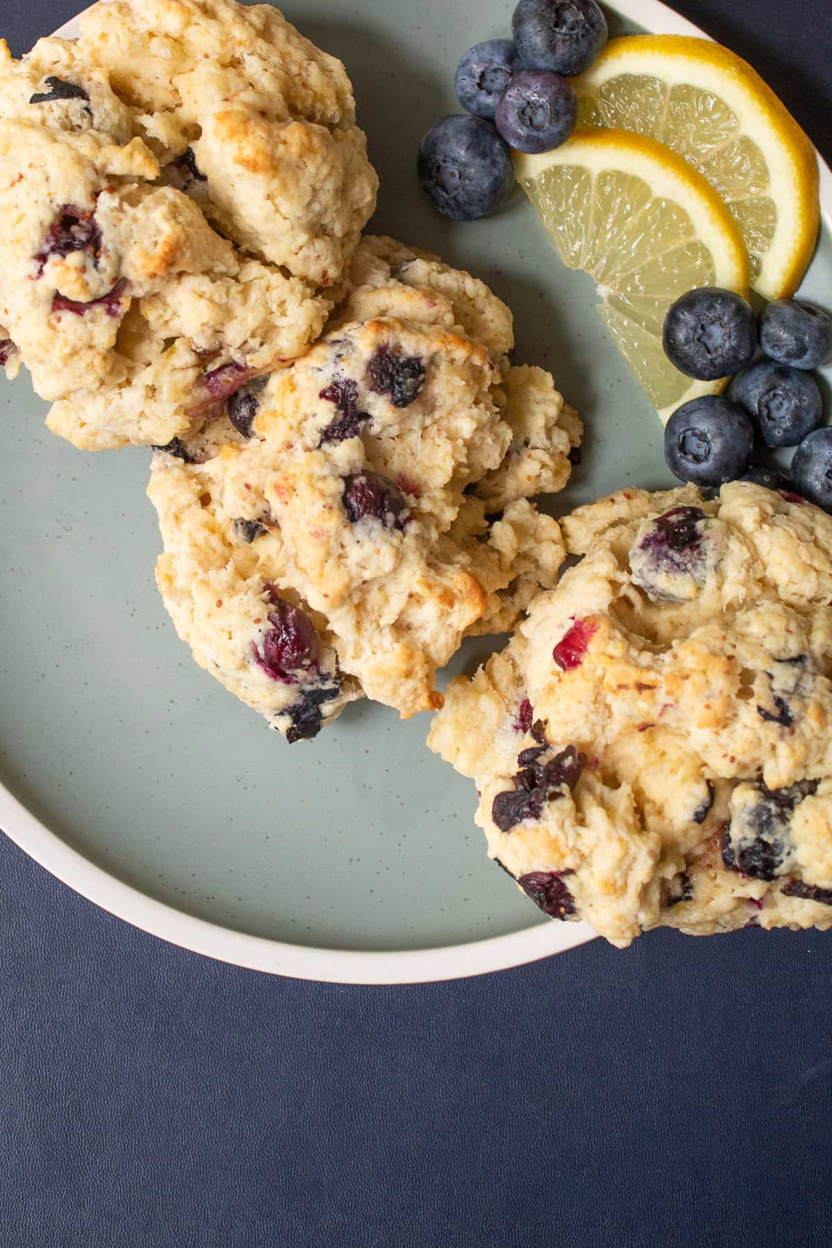 Three biscuits are plied on to a plate with fresh blueberries and lemon slices.