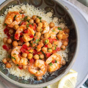 Lemon garlic shrimp are served over a bed of couscous in a green bowl.
