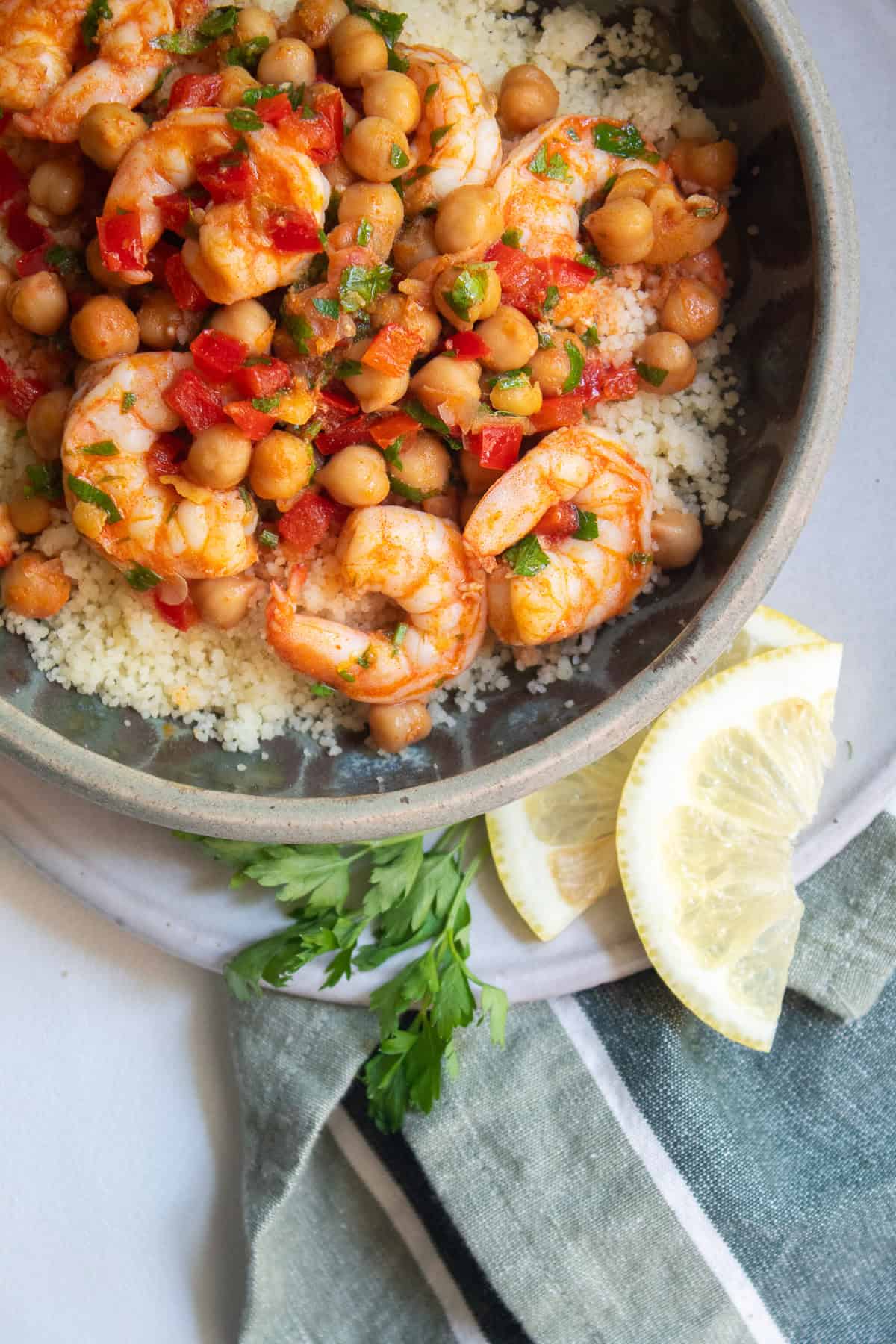 A bowl of lemon garlic shrimp is served alongside lemon and parsley garnish.