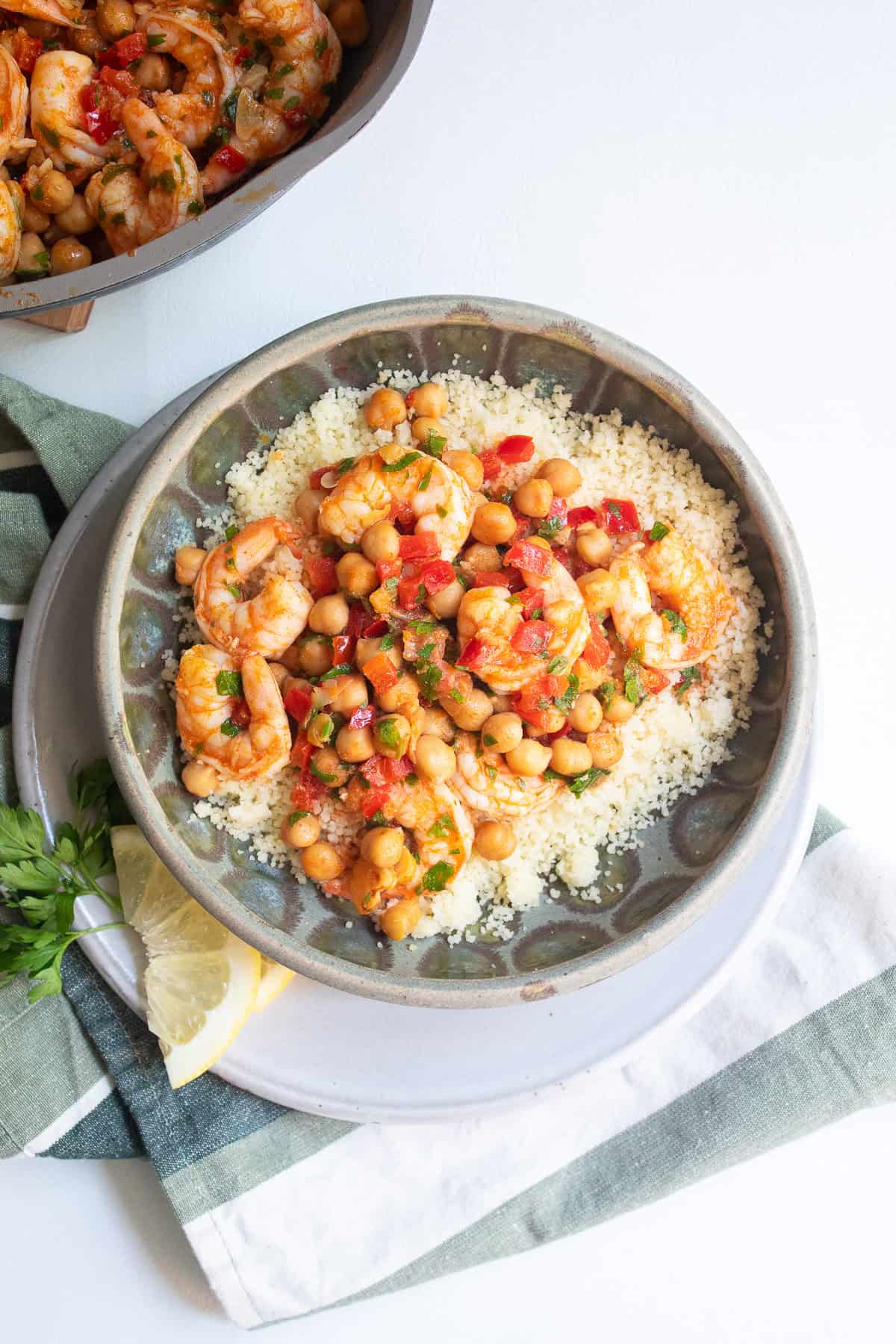 Lemon garlic shrimp are served over a bed of couscous in a green bowl next to sliced lemon and parsley leaves.