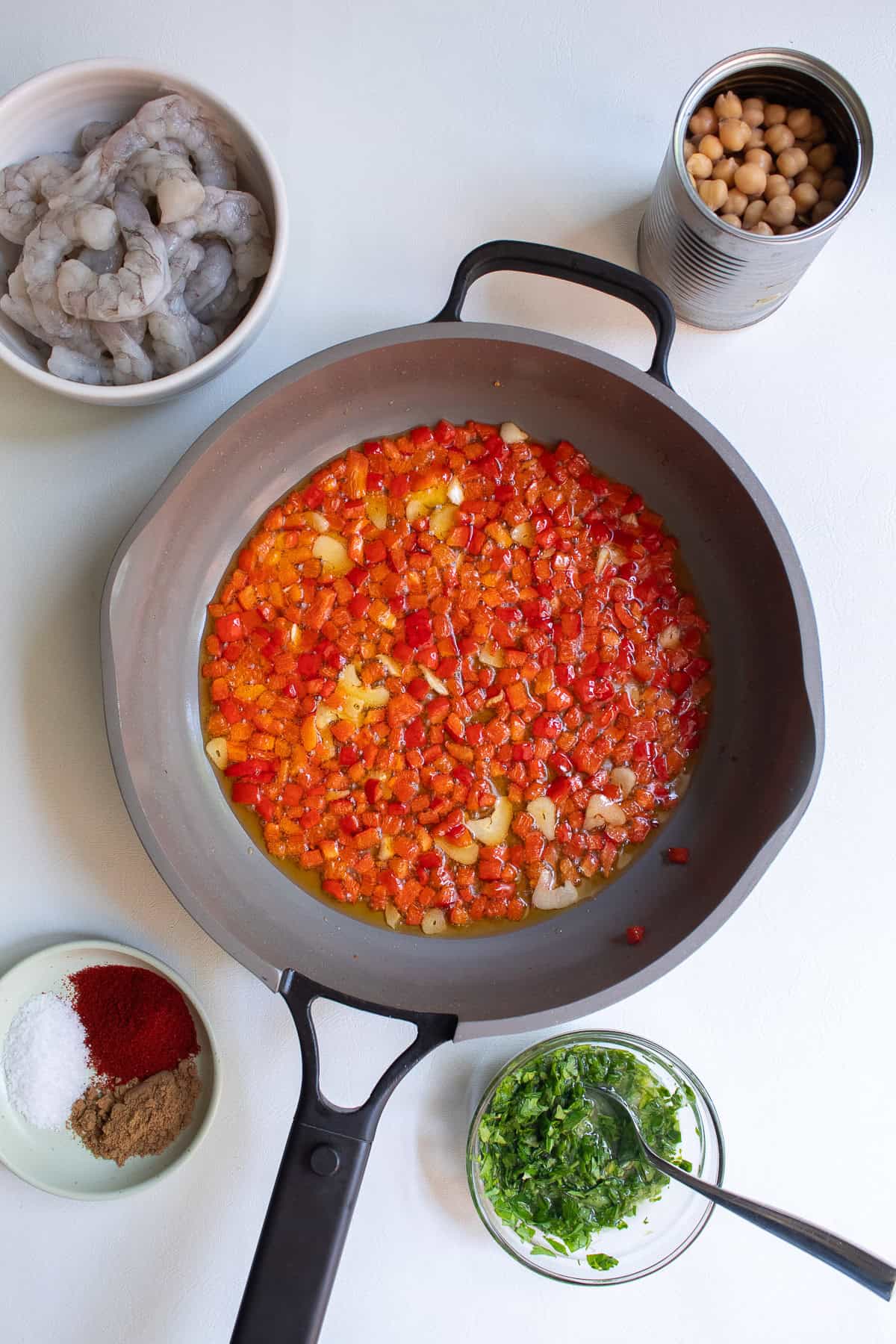 The garlic has softened and the bell peppers are bright red, turning the olive oil orange in the skillet.