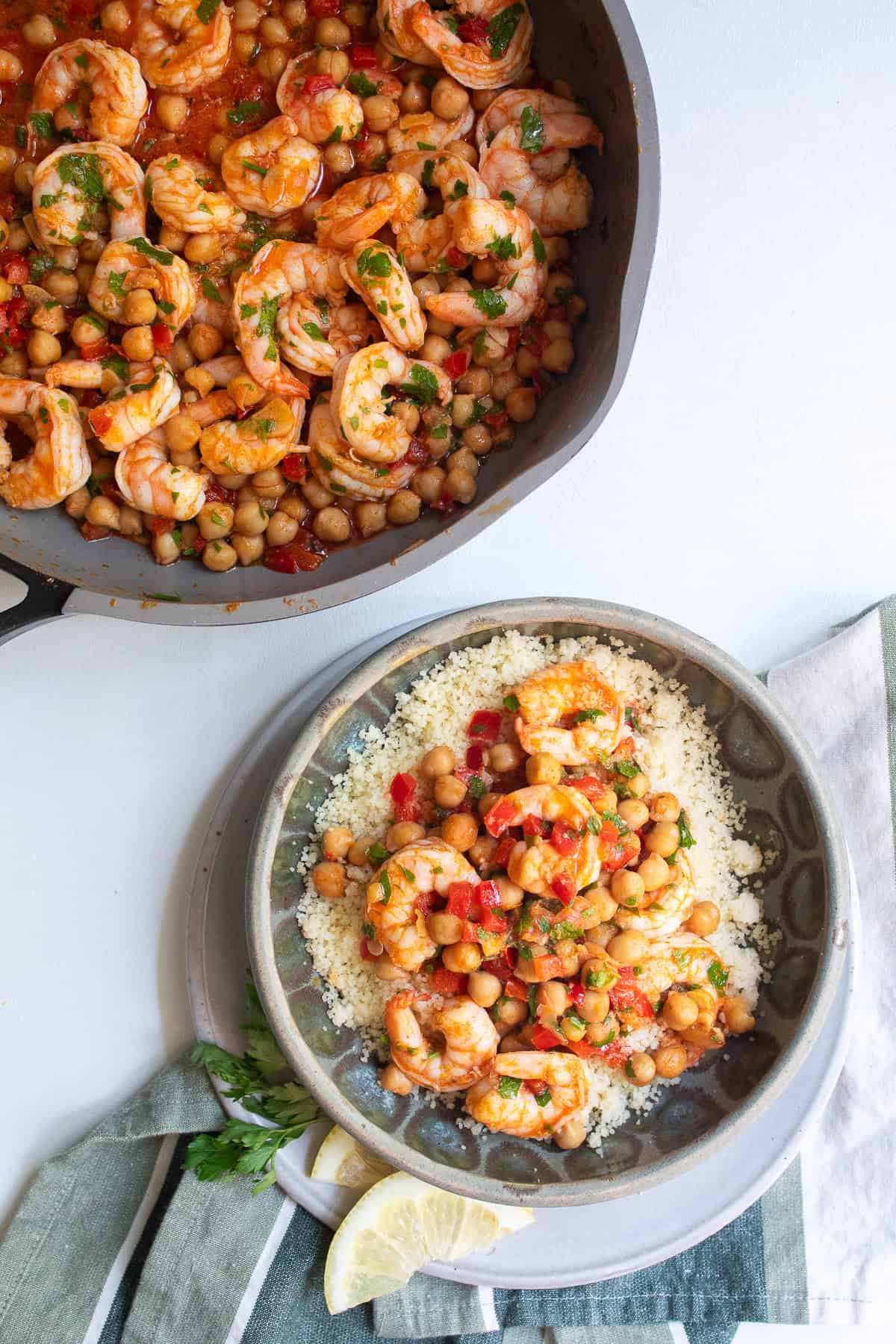 Lemon garlic shrimp are served over a bed of couscous in a green bowl alongside a skillet of the entree.
