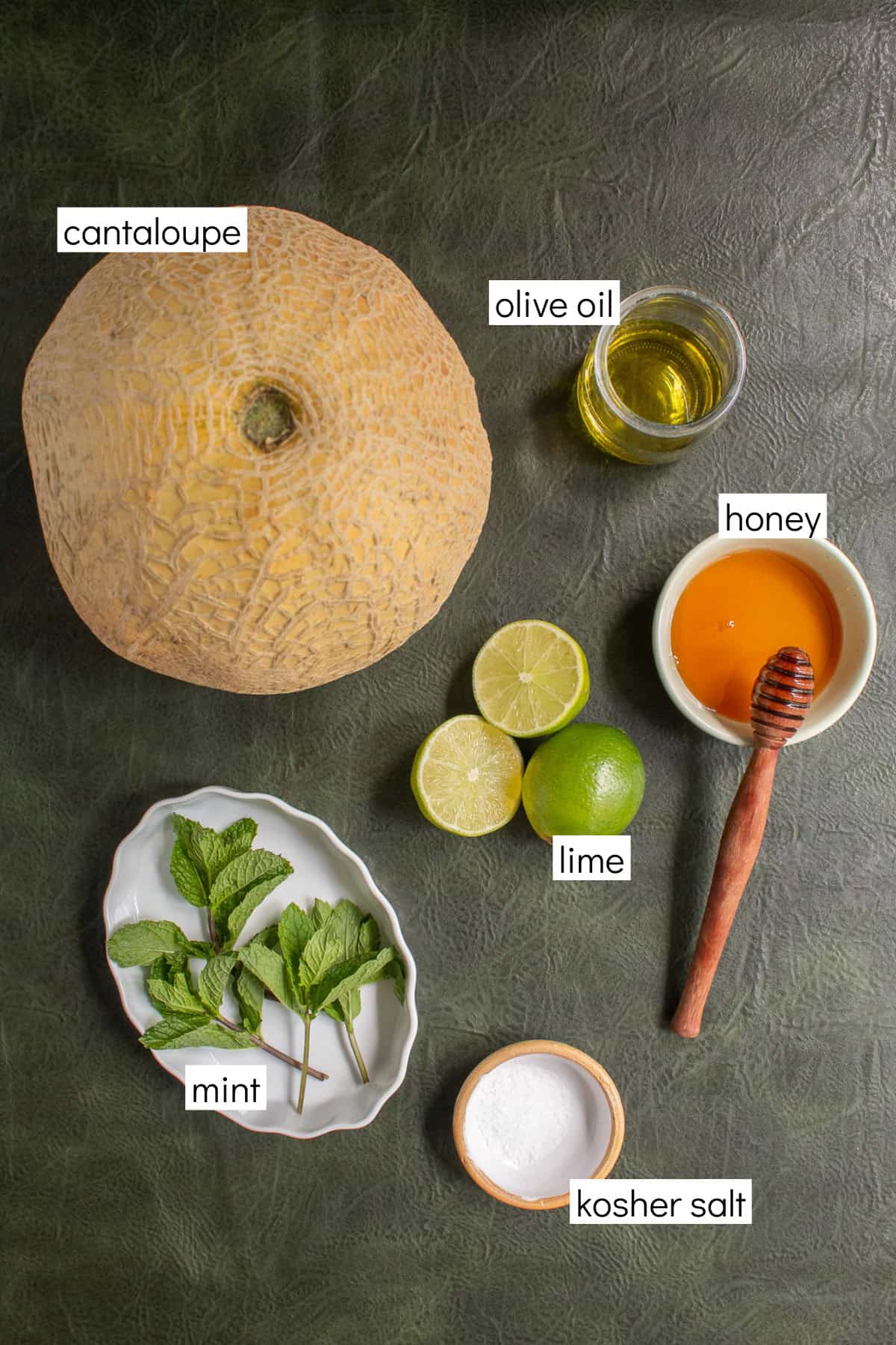 Ingredients for the recipe are displayed and labeled with white text boxes including the words cantaloupe, olive oil, honey, lime, mint, and kosher salt.
