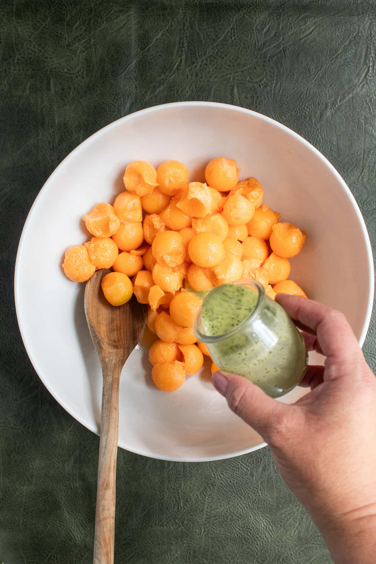 The dressing is poured over melon balls in a white bowl.
