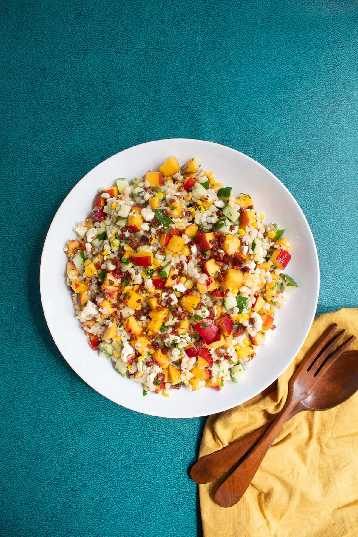 The finished salad is served on a white platter next to wooden salad servers.