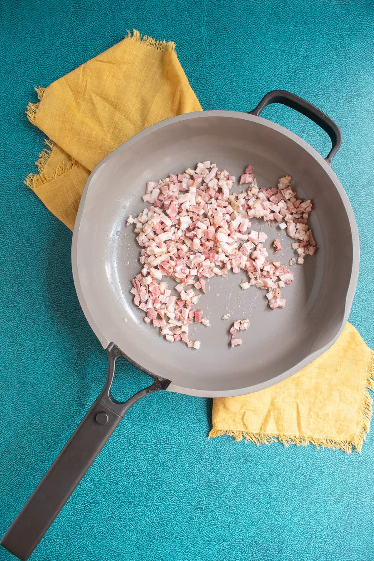 Pancetta is added to a light colored skillet.