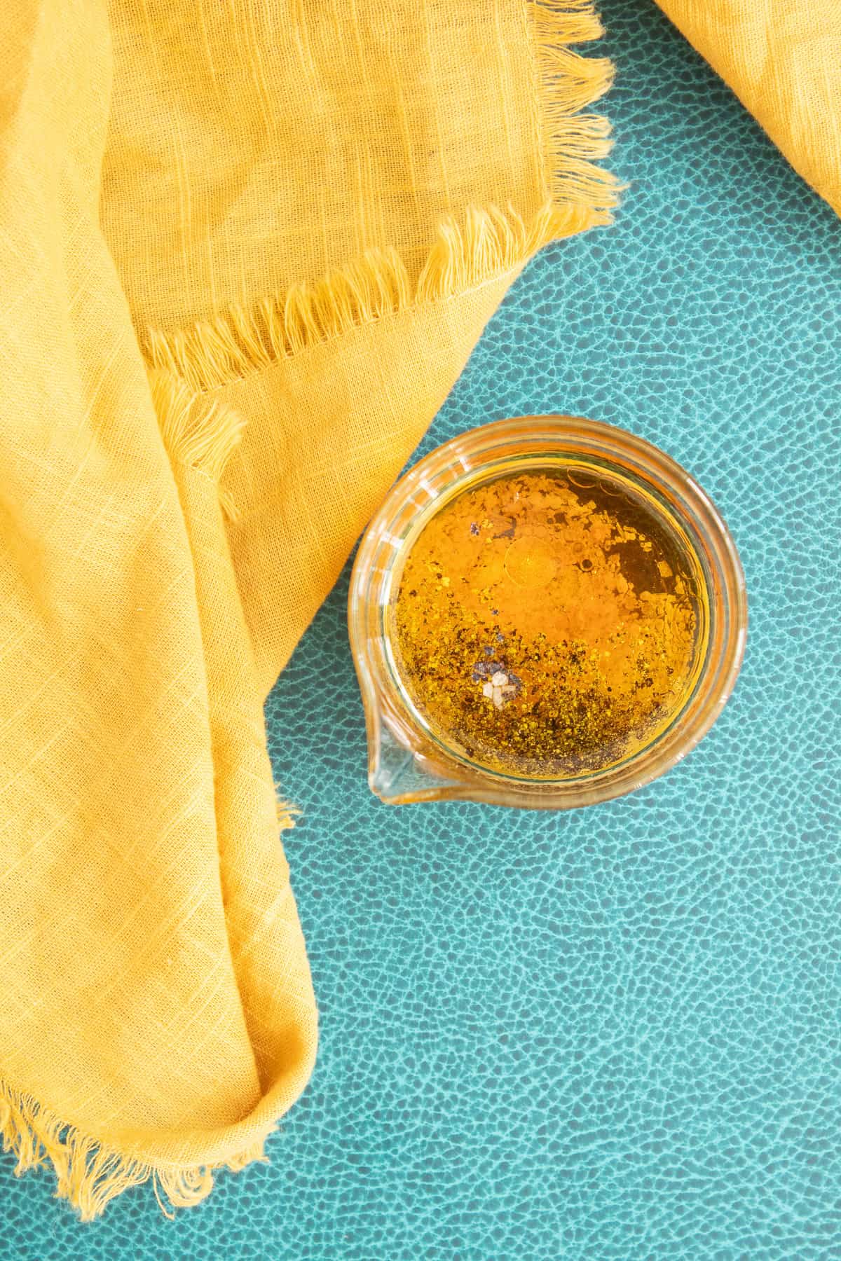 Olive oil, salt, pepper, and vinegar are added to a small glass beaker.