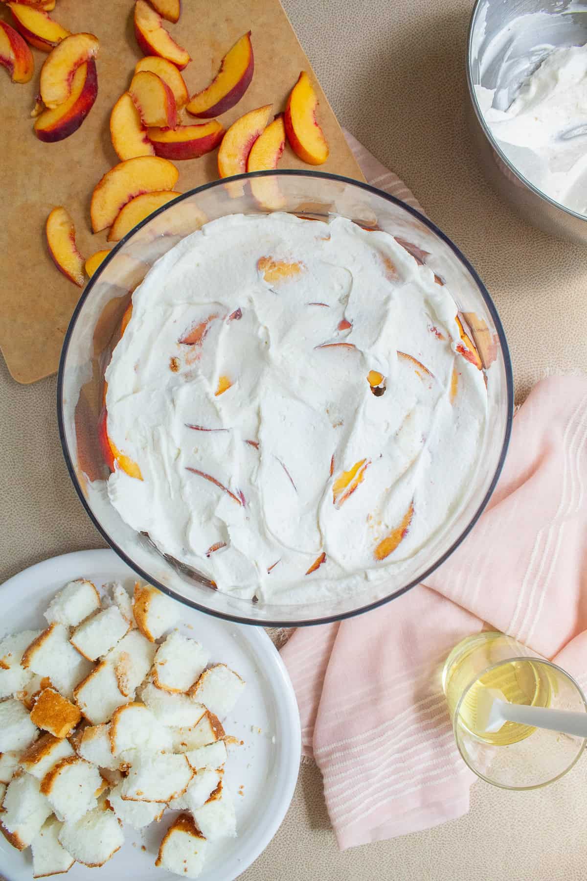 Whipped cream is spread out over the peaches, right to the edges of the trifle bowl.