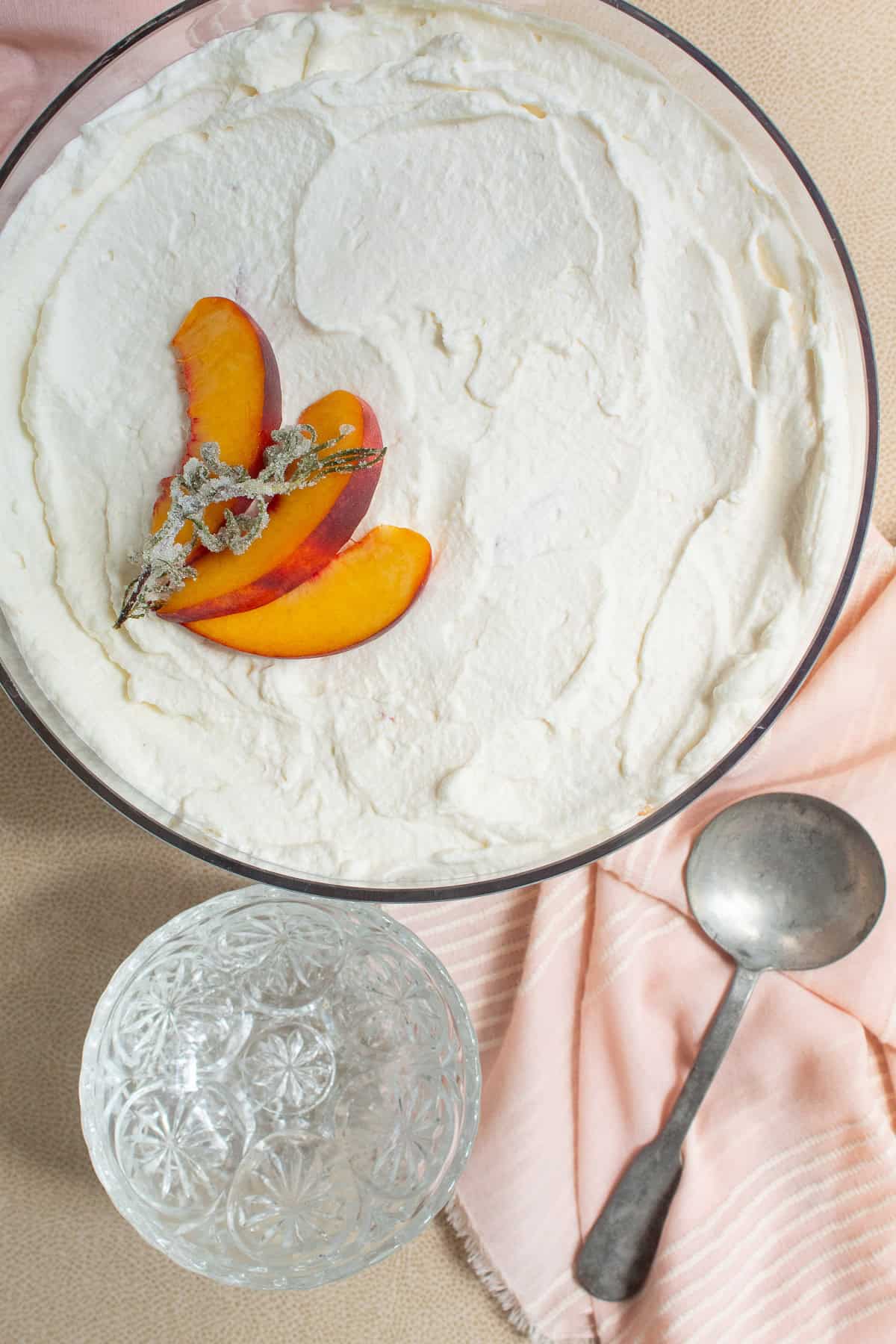 The finished trifle is garnished with candied rosemary and peach slices and served in glass dessert bowls.