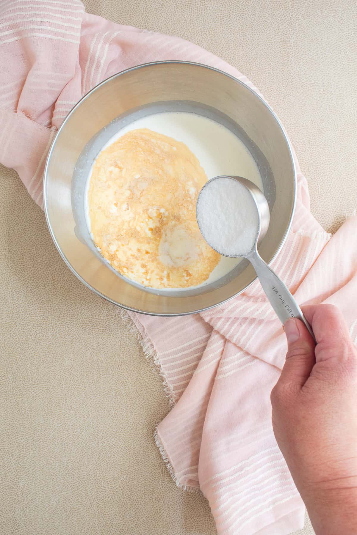Sugar is added to a bowl that contains heavy cream and vanilla.