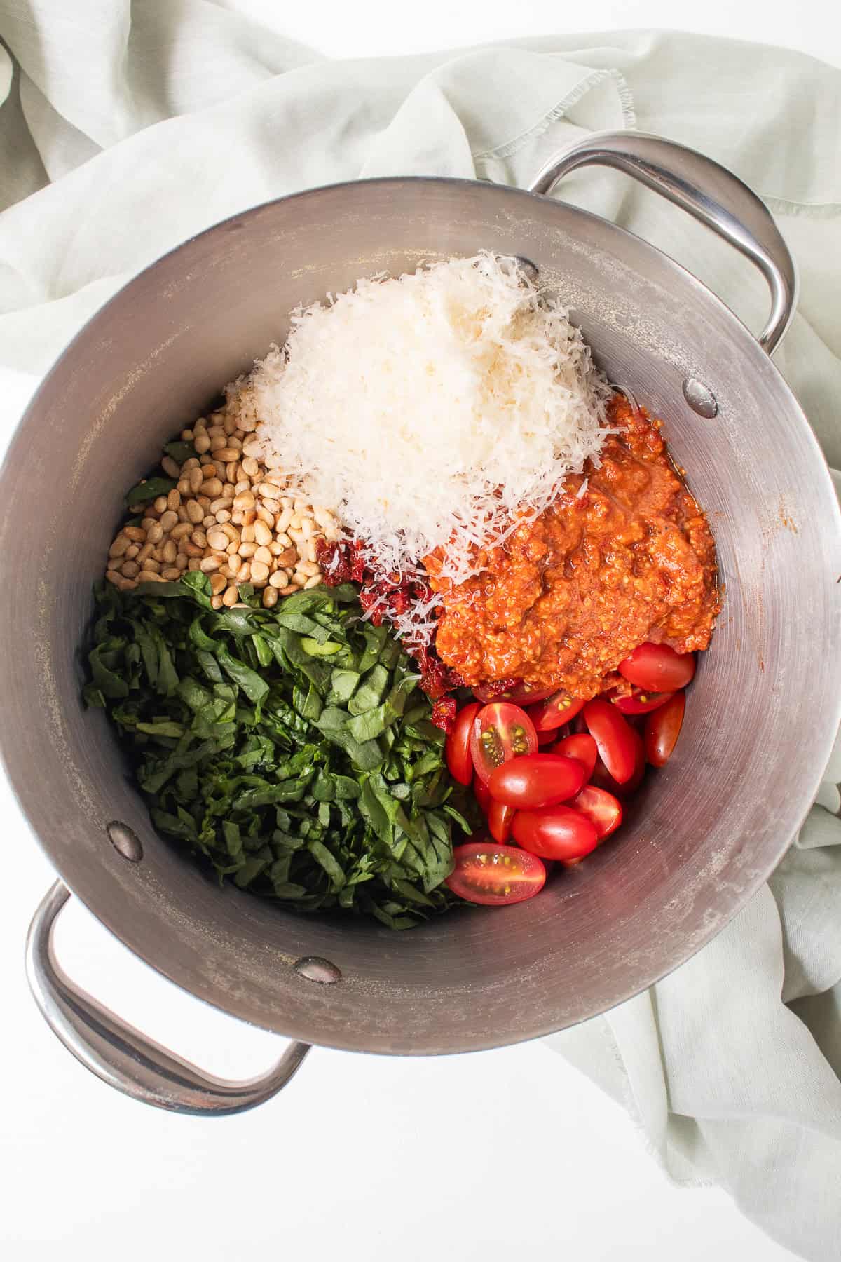 Shredded spinach, pine nuts, Parmesan, red pesto, and fresh tomatoes are piled back into the pot with the cooked pasta.