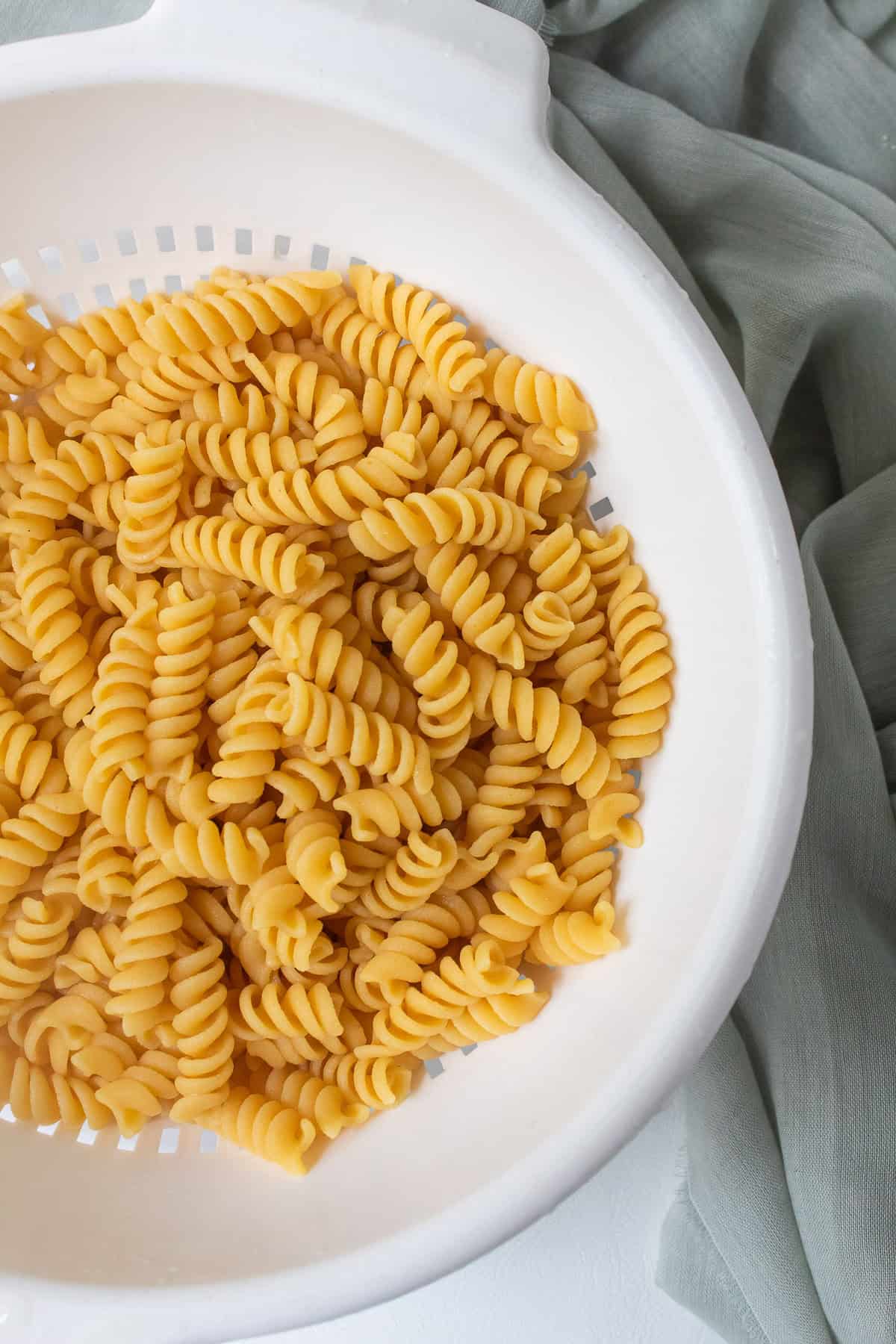 Cooked pasta is drained in a white colander.