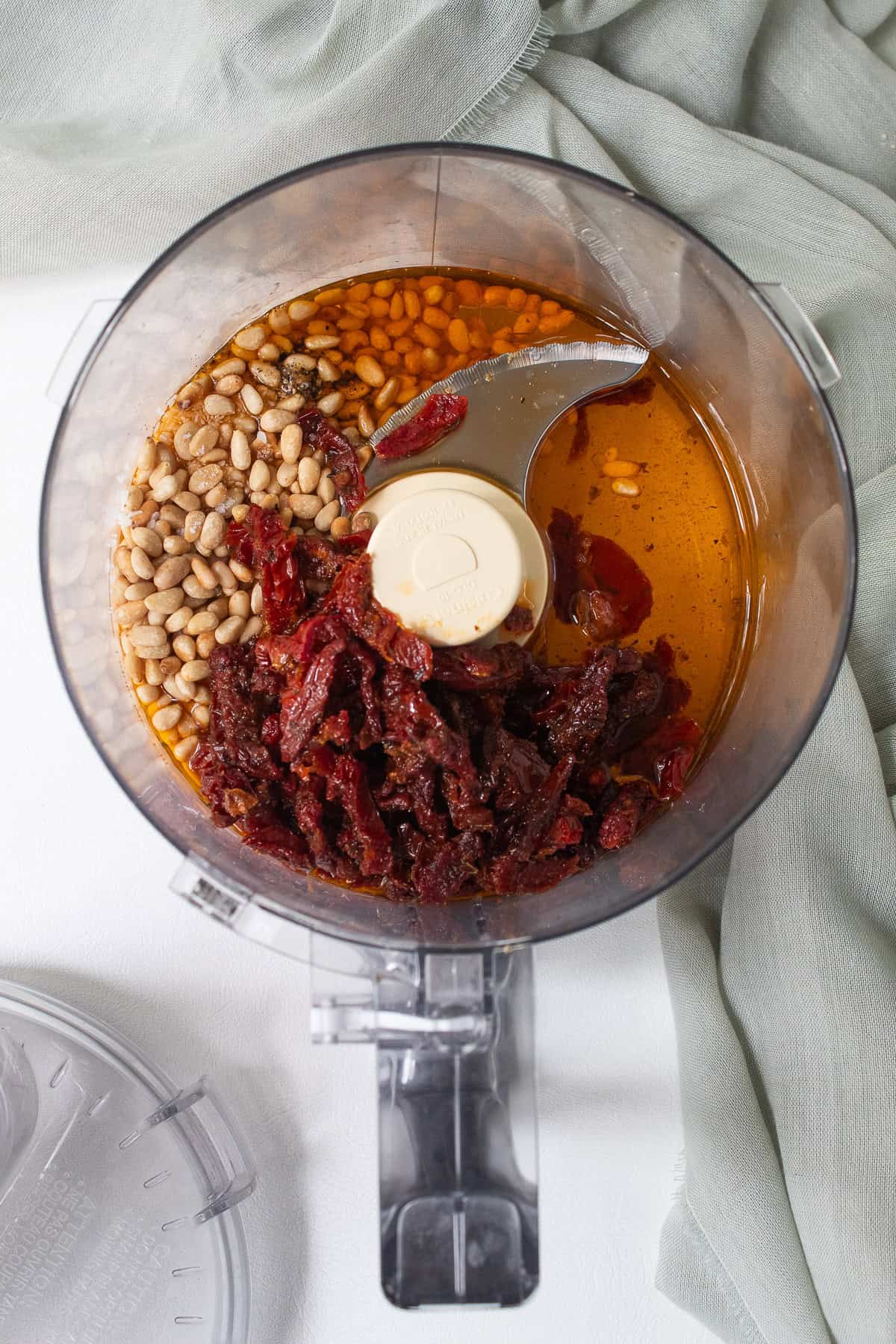Toasted pine nuts, salt, pepper, sun dried tomatoes, and olive oil are added to a food processor bowl.