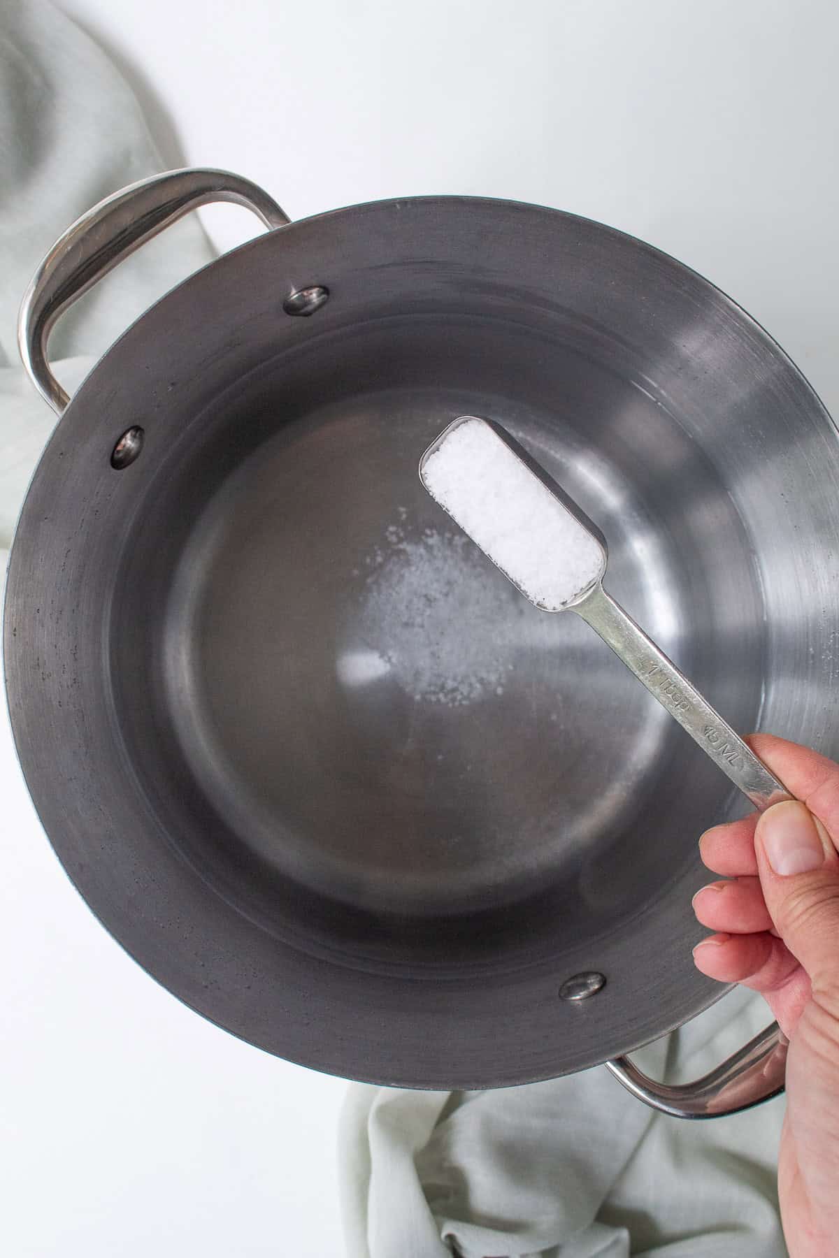 Kosher salt is sprinkled into the pasta cooking water.