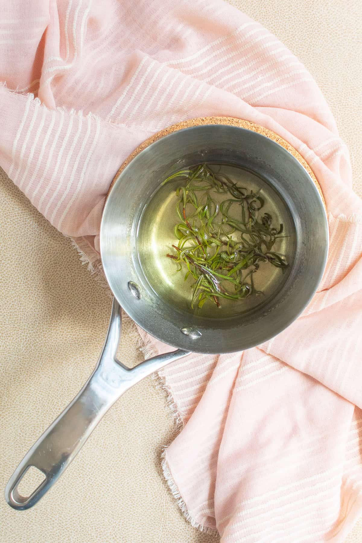 The rosemary syrup steeps in a saucepan, taking on a pale yellow-green color.