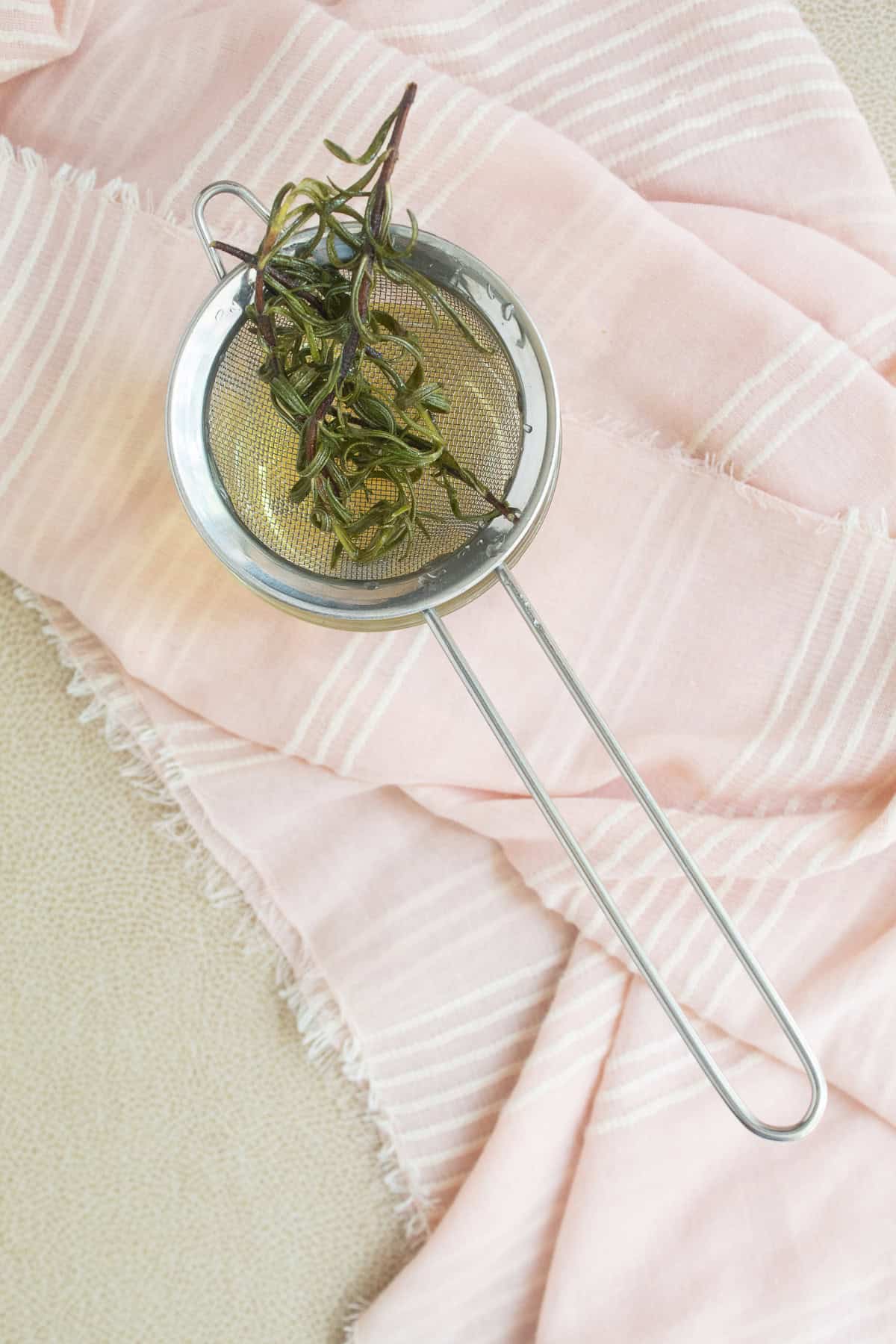 The rosemary syrup is strained over a mesh strainer into a glass.