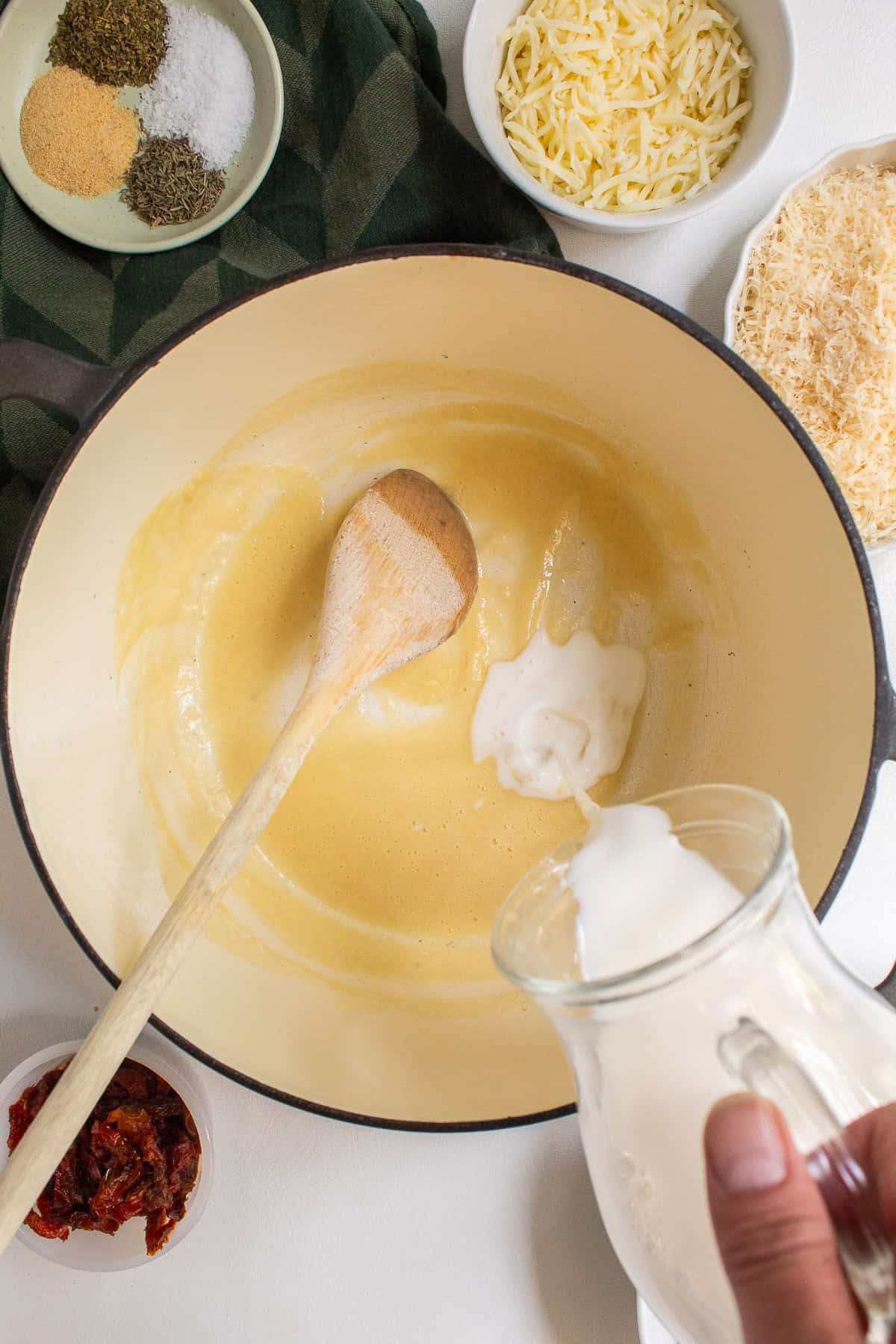 Milk is slowly streamed into the roux from a pitcher.
