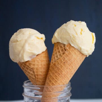 Two scoops of sweet corn ice cream sit in sugar cones.