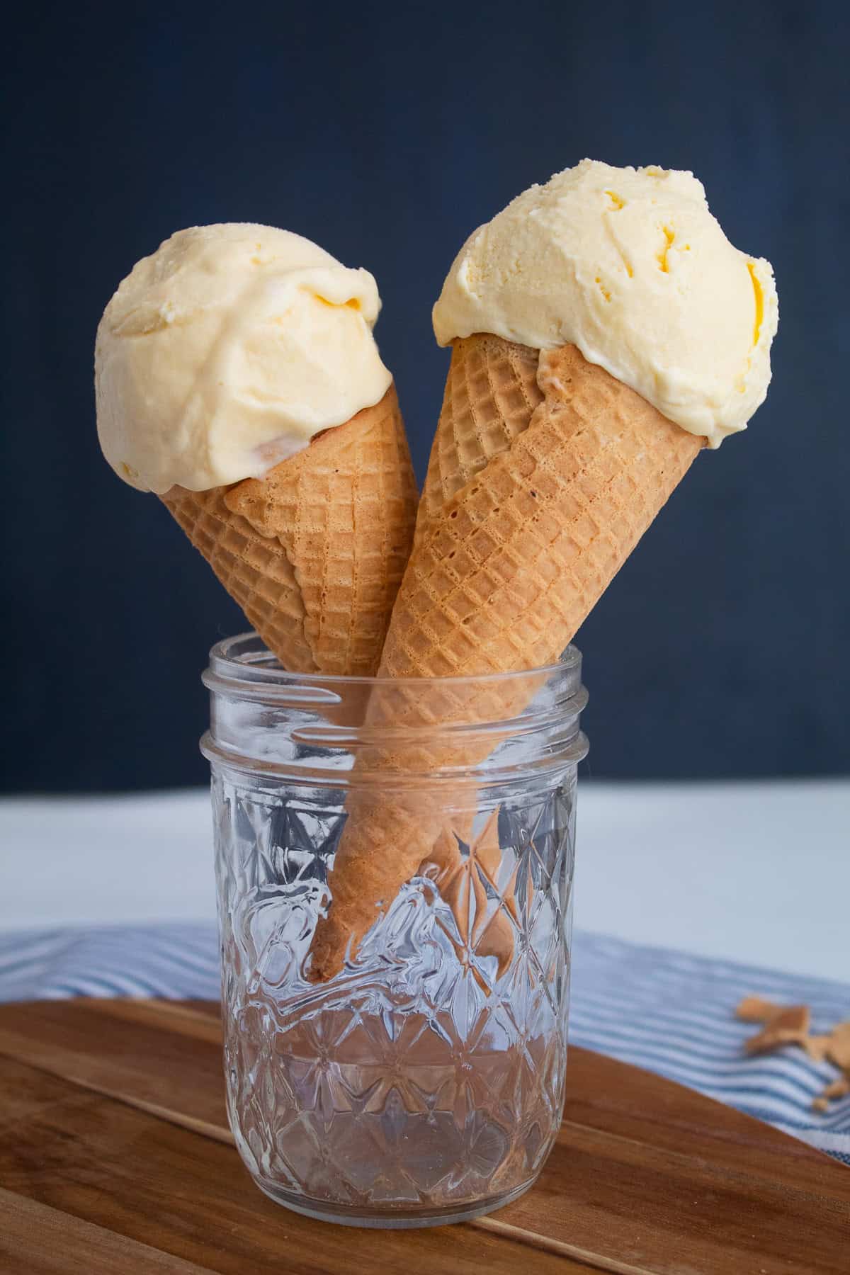 Two sugar cones are topped with scoops of a pale yellow ice cream.