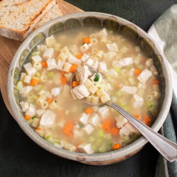 A spoonful of chicken noodle soup contains chunks of chicken breast, ditalini noodles, carrots, and celery.