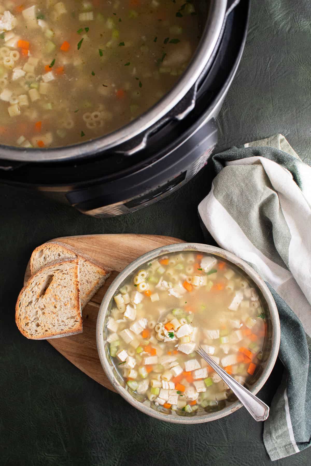 A bowl of soup with ditalini noodles, chicken chunks, carrots, and celery is served with toasted bread.