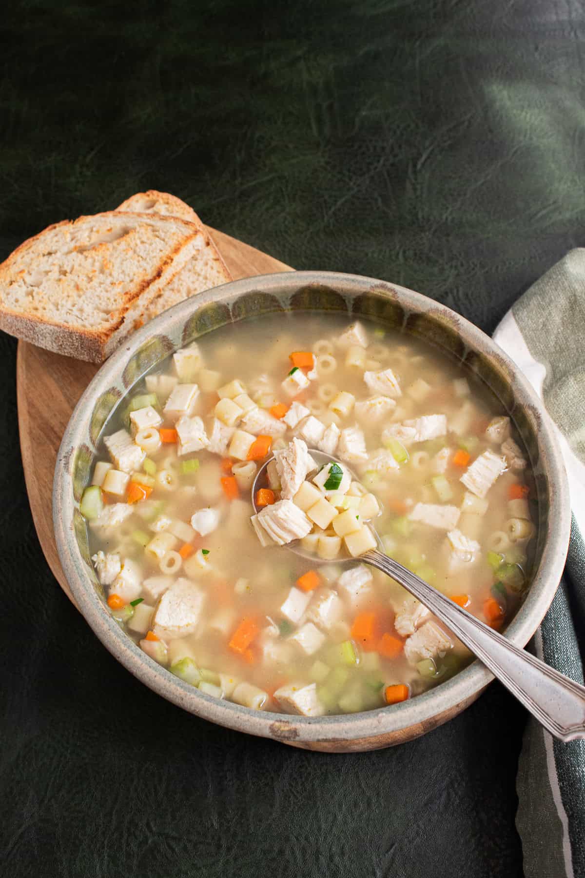 Chicken noodle soup in a green and gray ceramic bowl sits on a green background.