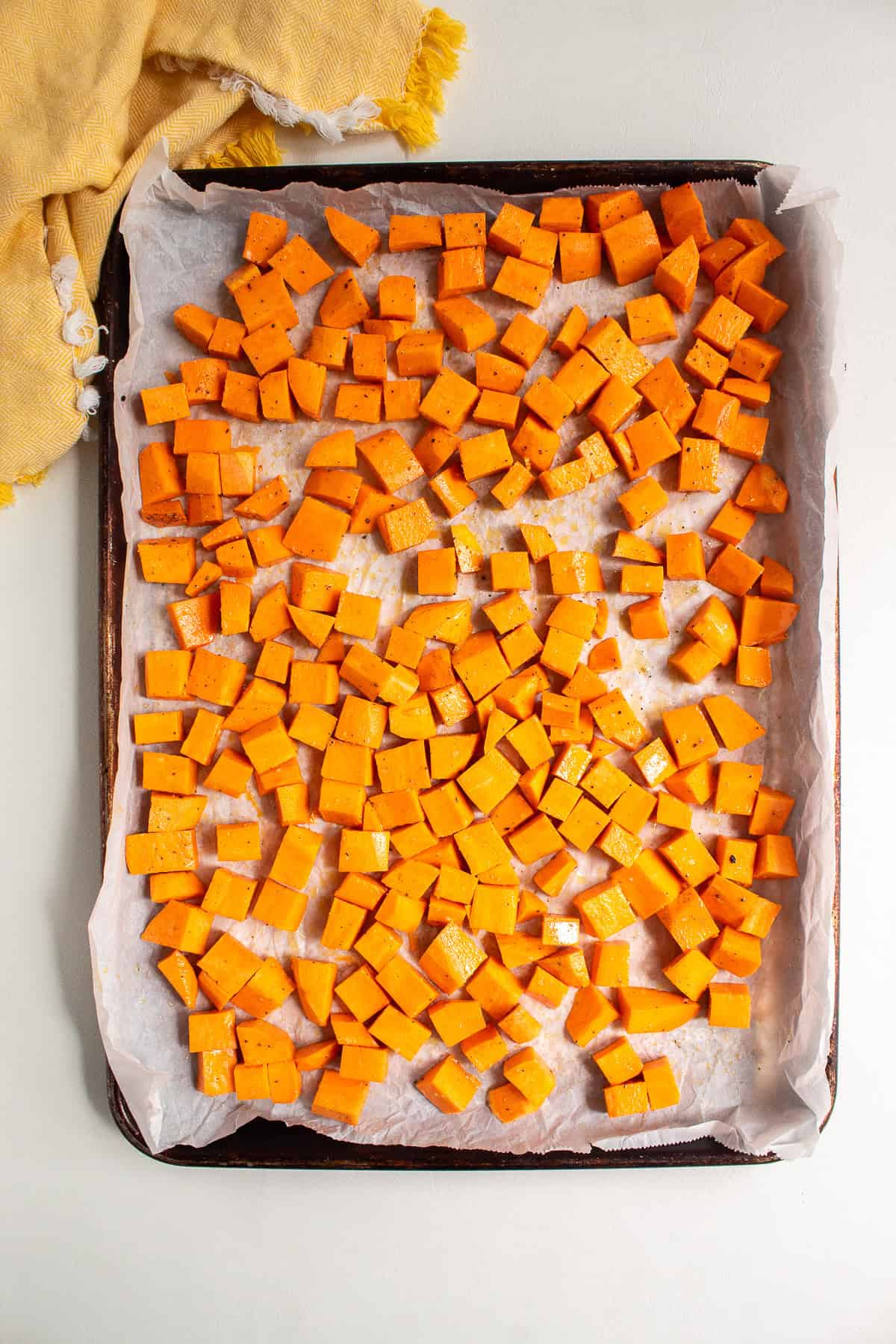 Cubes of sweet potato are oiled and seasoned with salt and pepper on a sheet pan.