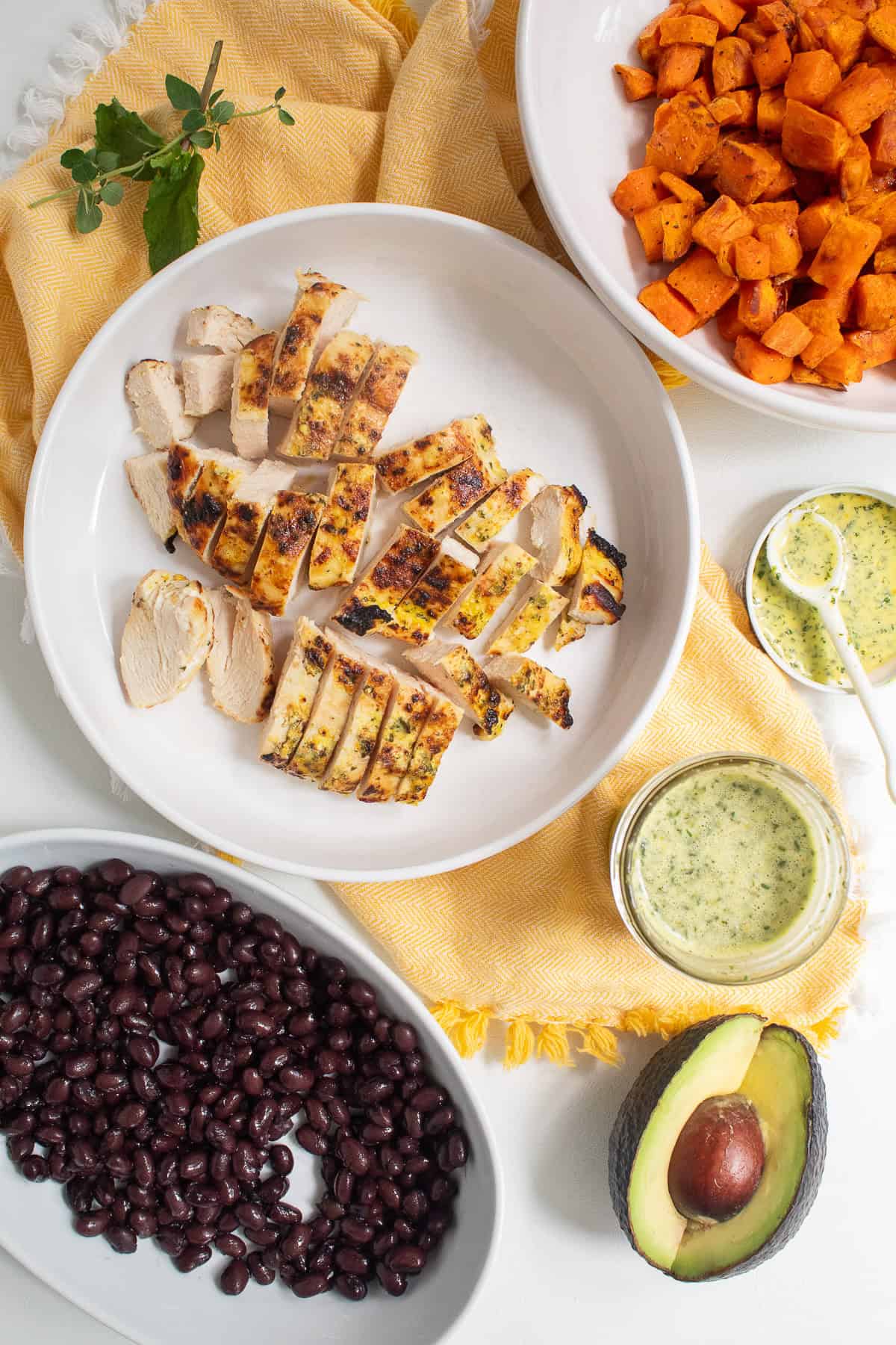 All of the bowl components are laid out on a yellow and white surface for building the chicken bowls.