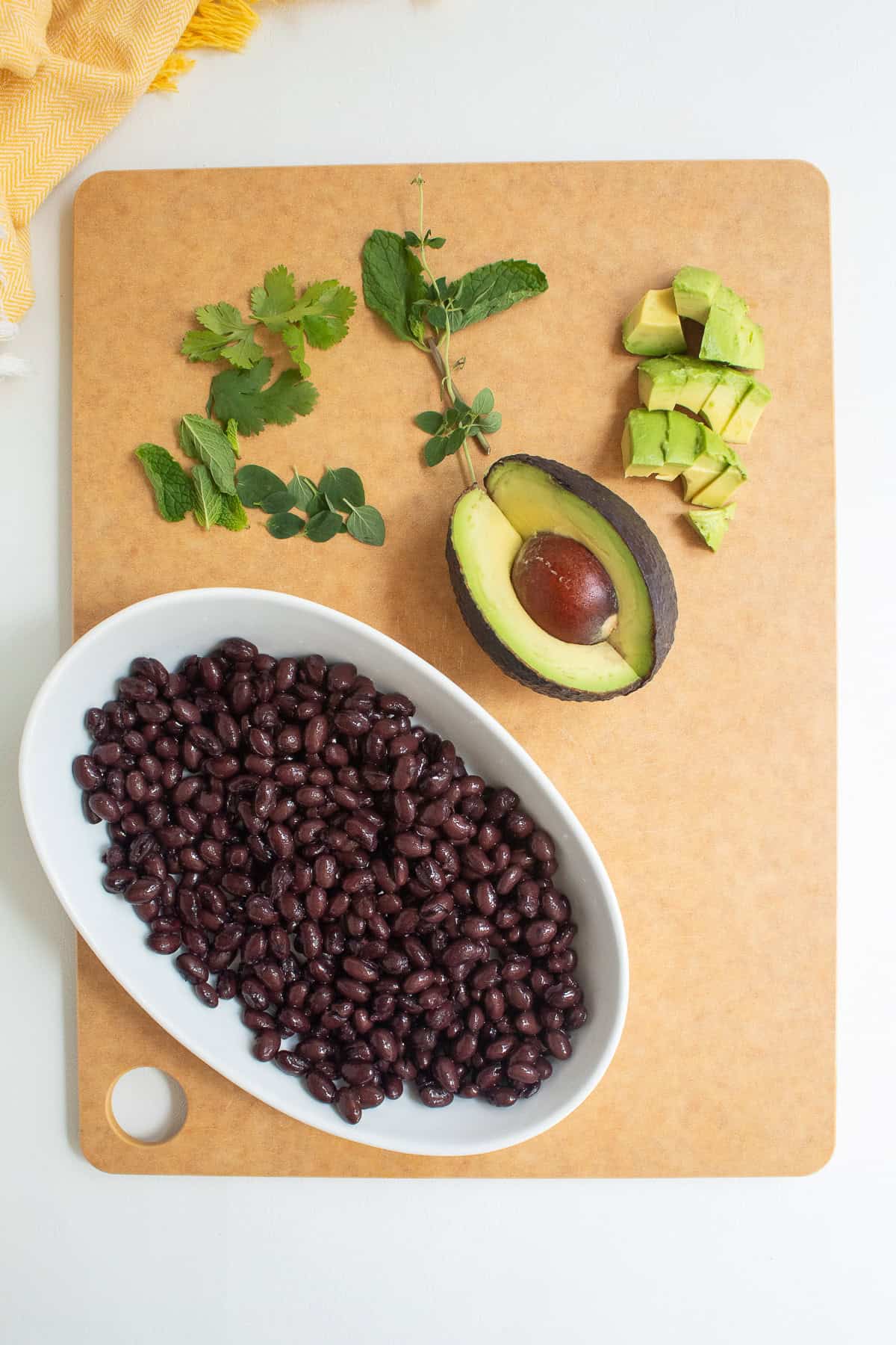 Canned black beans are heated in a bowl while herbs and avocado are prepared for bowl toppings.