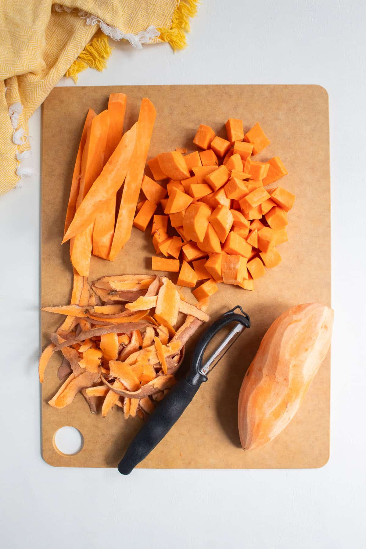 Sweet potatoes are peeled, sliced into sticks, and cubed on a brown cutting board.