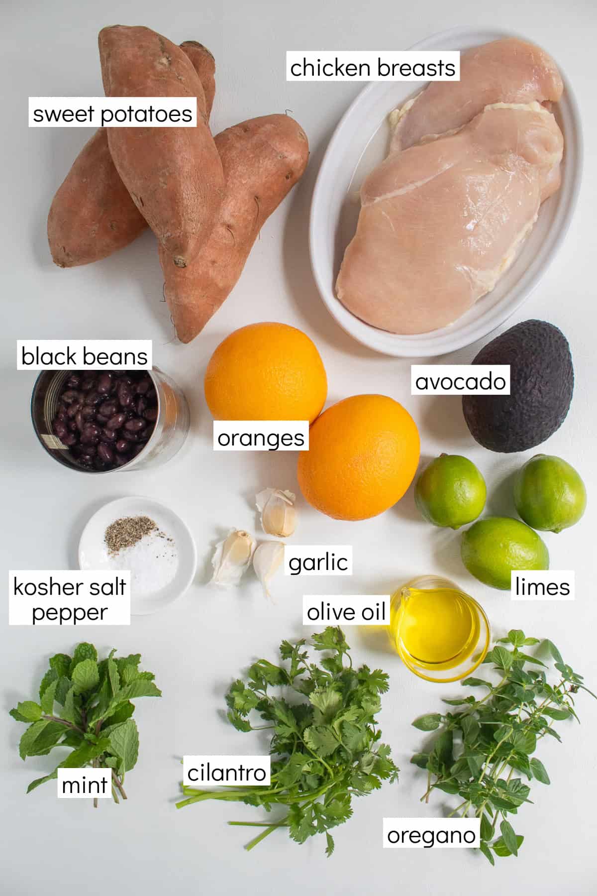 Ingredients for the recipe are displayed and labeled with white text boxes including the words sweet potatoes, chicken breasts, black beans, oranges, avocado, kosher salt, black pepper, garlic, limes, olive oil, mint, cilantro, and oregano.