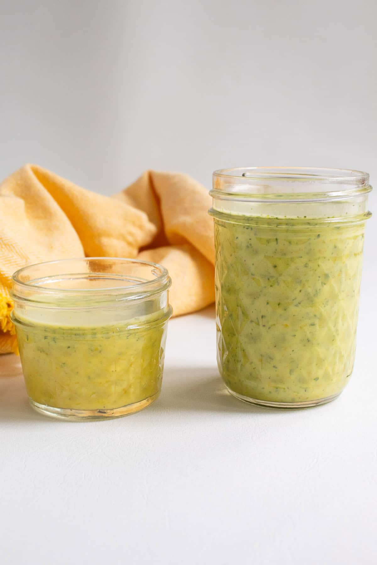 Two sauces are next to one another in jars with an orange-hued marinade and a greener mojo sauce.