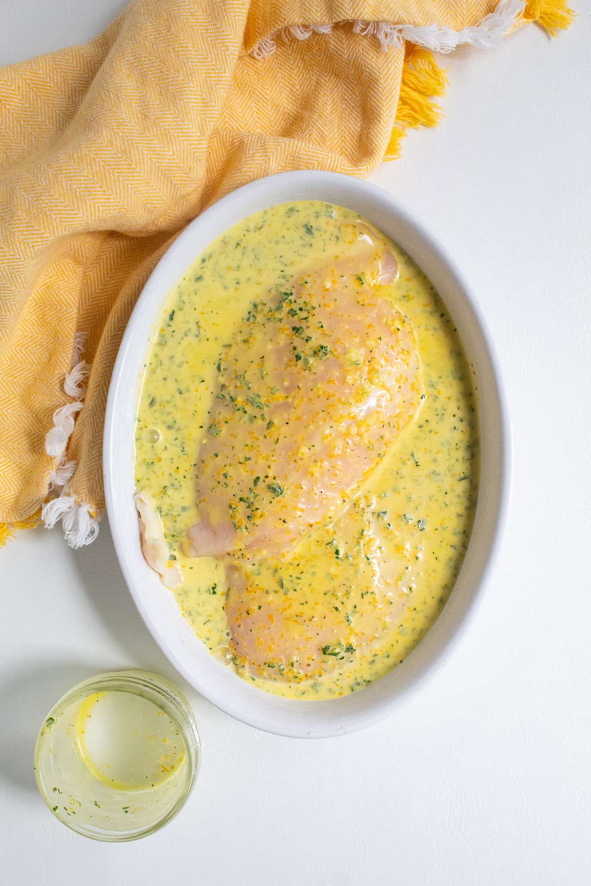 The chicken breasts are marinated in a shallow bowl.