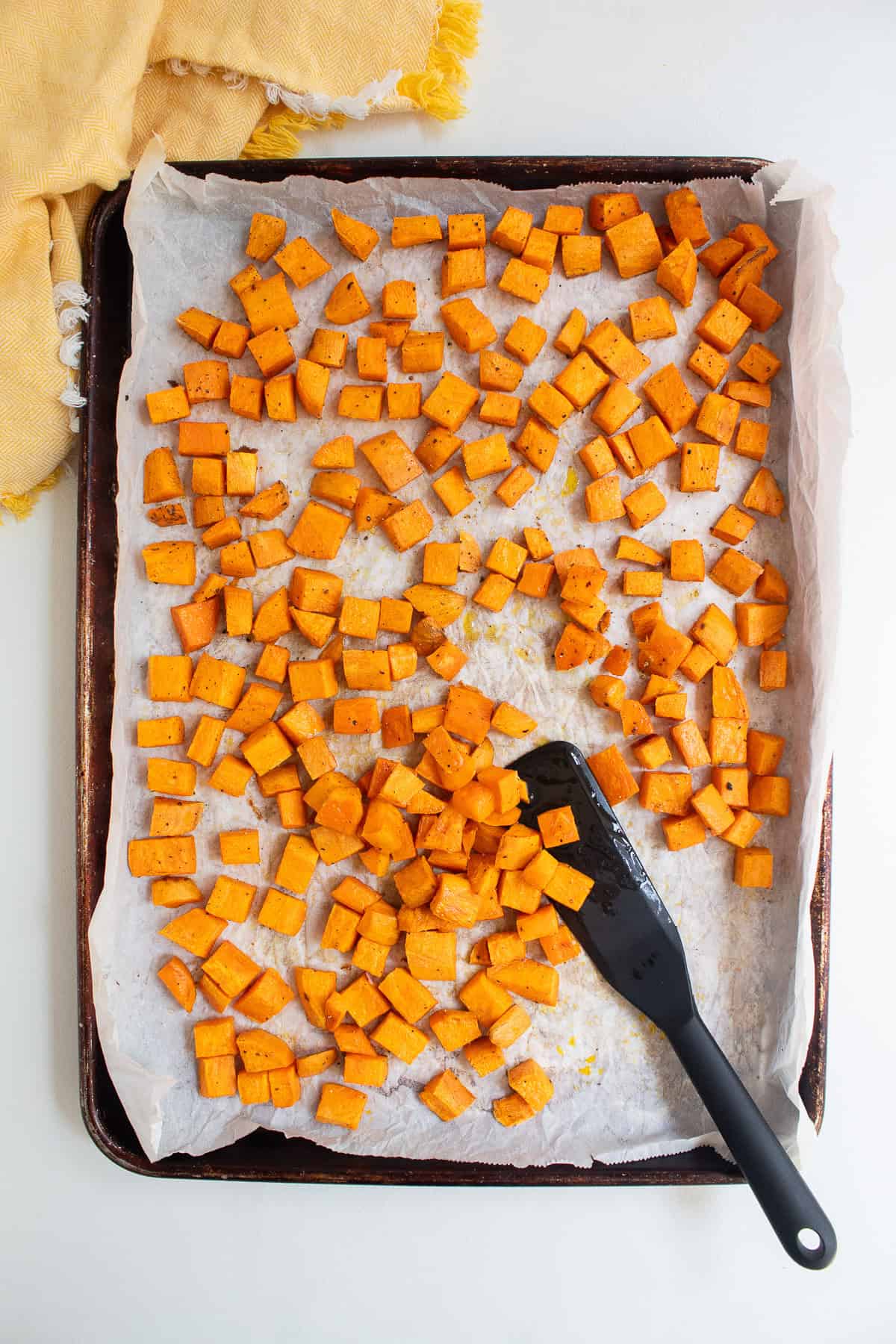 Cubes of sweet potato are roasted with golden edges on a parchment lined sheet pan.