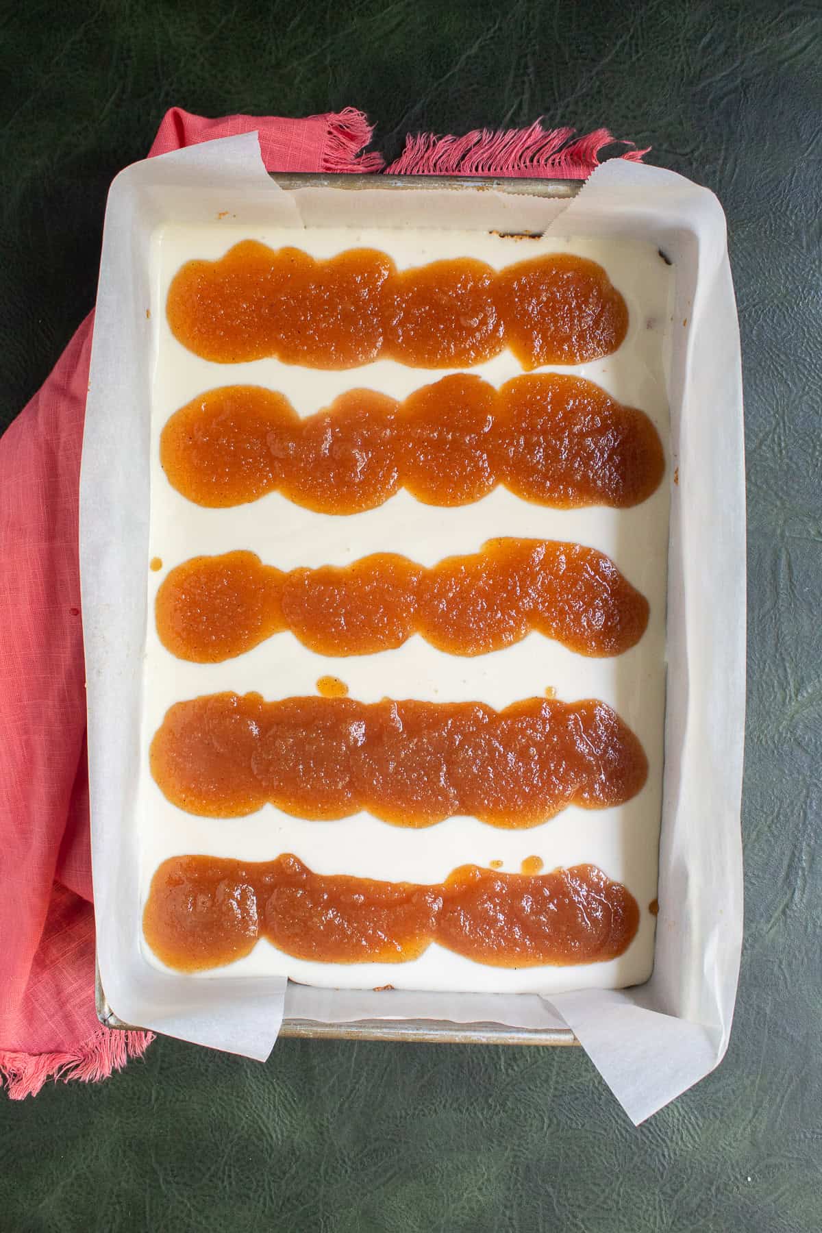 Lines of applesauce filling are spooned over the cheesecake filling.