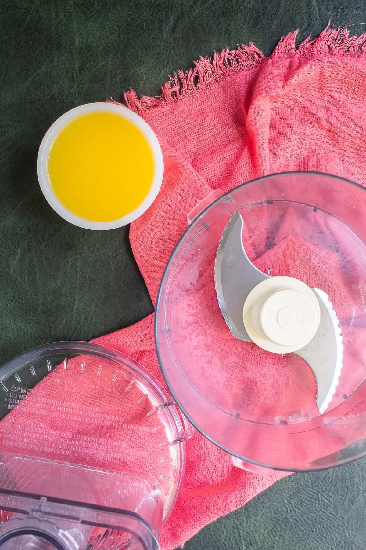 Melted butter sits in a small bowl next to a food processor bowl.