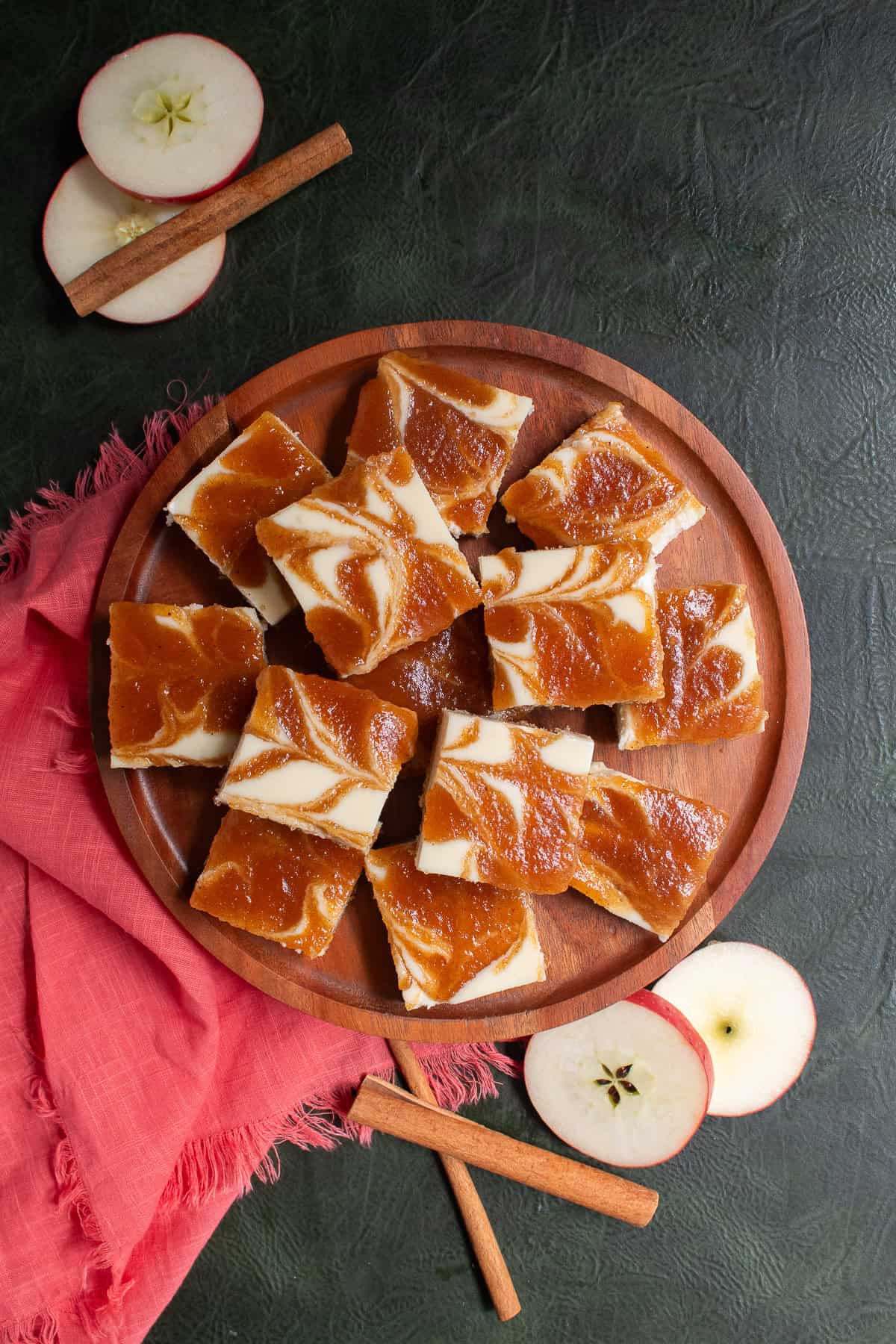 Cheesecake bars are piled high on a wooden platter next to a coral colored napkin.