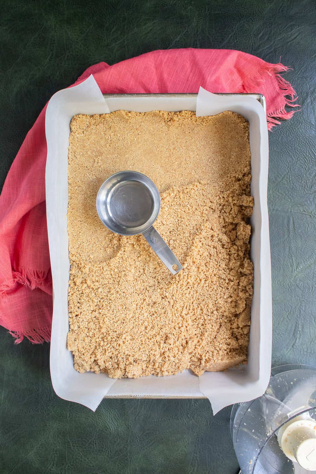 The graham cracker crumbs are pressed into the bottom of the baking pan with the flat bottom of a measuring cup.