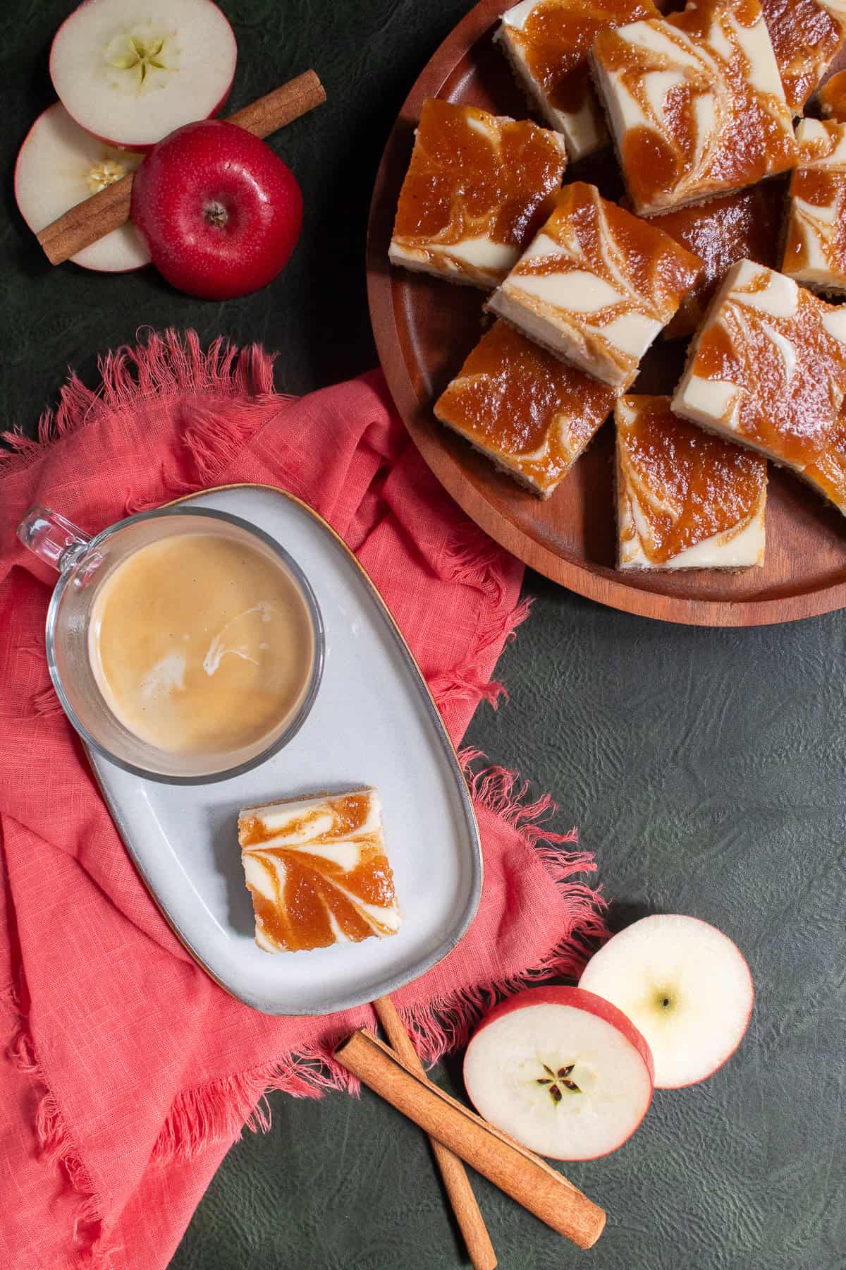 One apple cheesecake bar is served alongside a cup of milky coffee on a small plate.