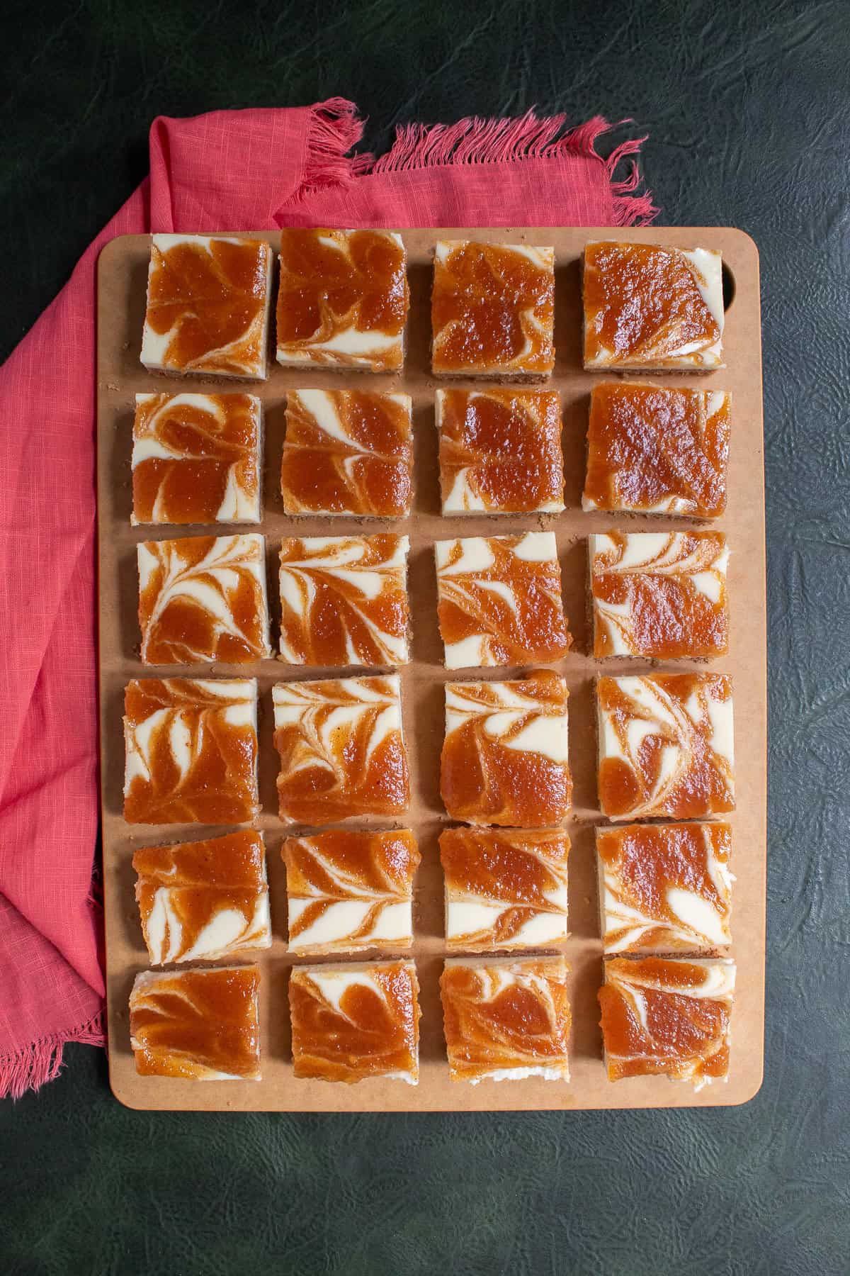The slices cheesecake bars are arrayed on a large cutting board.