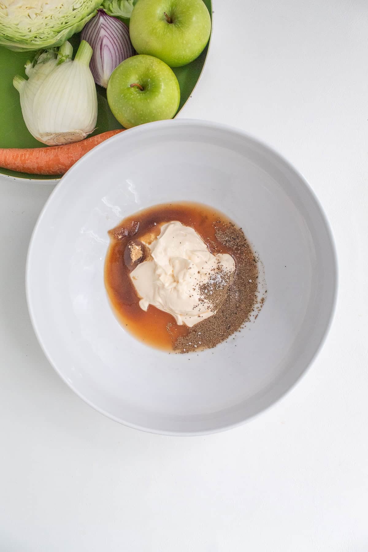 Ingredients for the dressing, including black pepper , mayonnaise, apple cider vinegar, and celery seeds, are added to the mixing bowl.