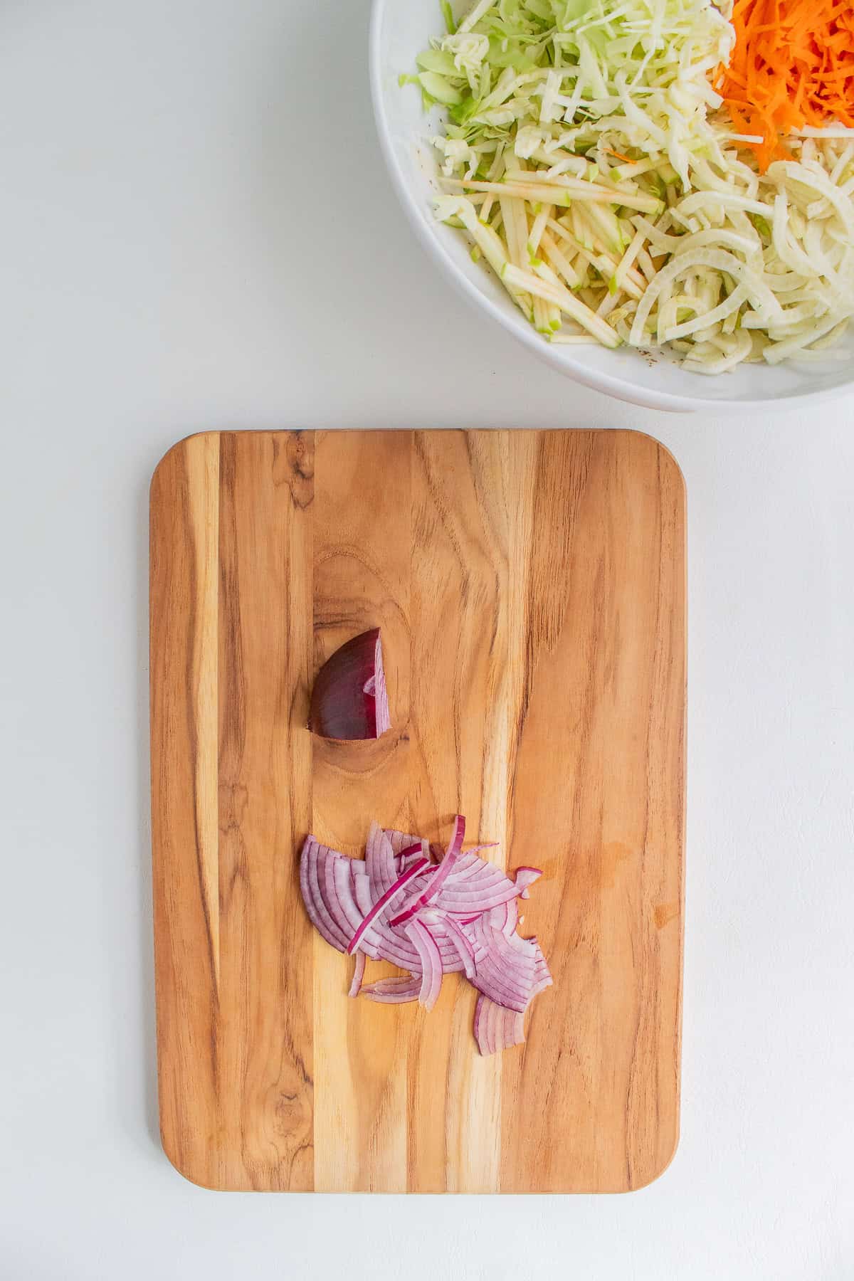 Red onion is sliced into thin strips on a wooden cutting board.