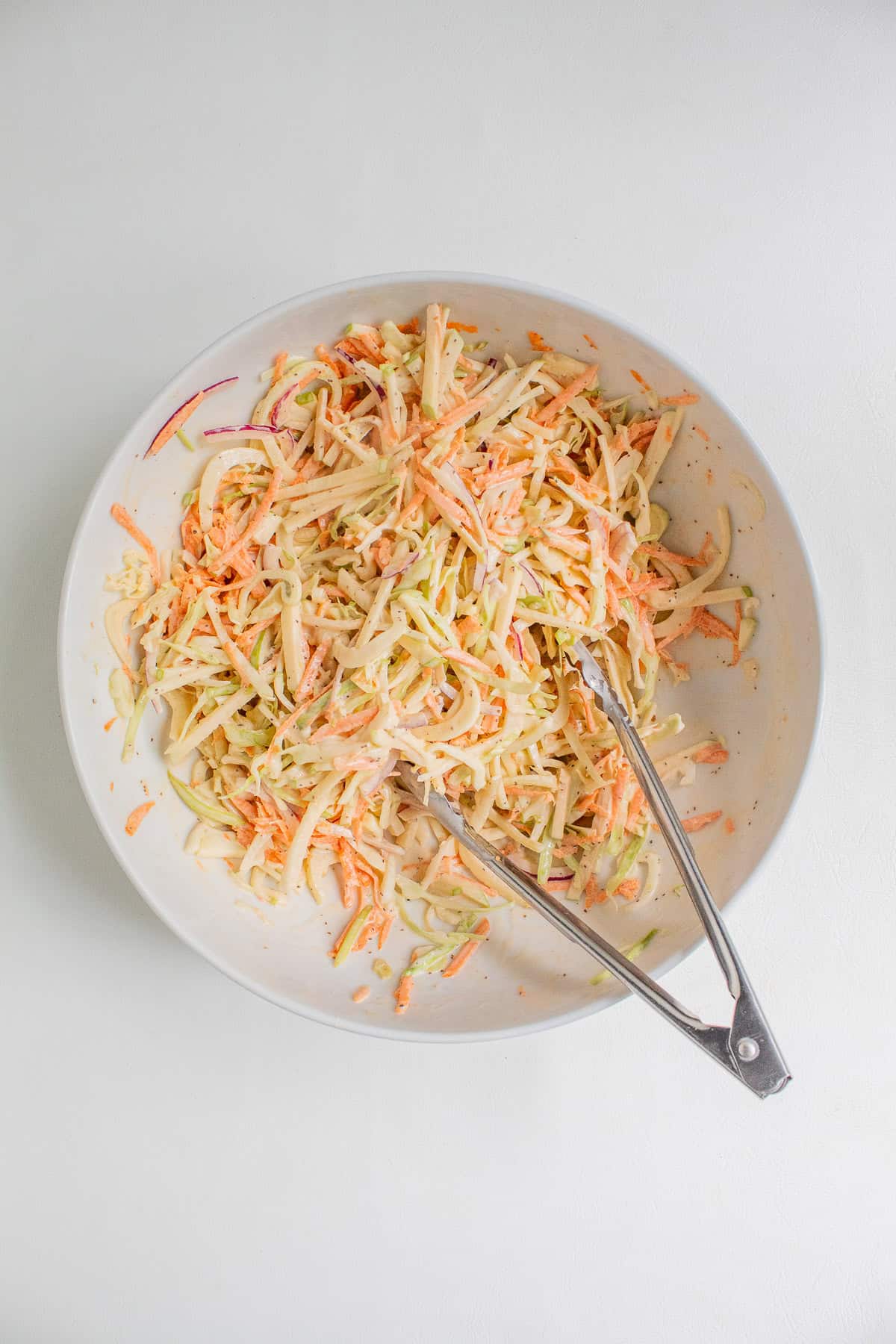 The slaw is tossed with the dressing using tongs.