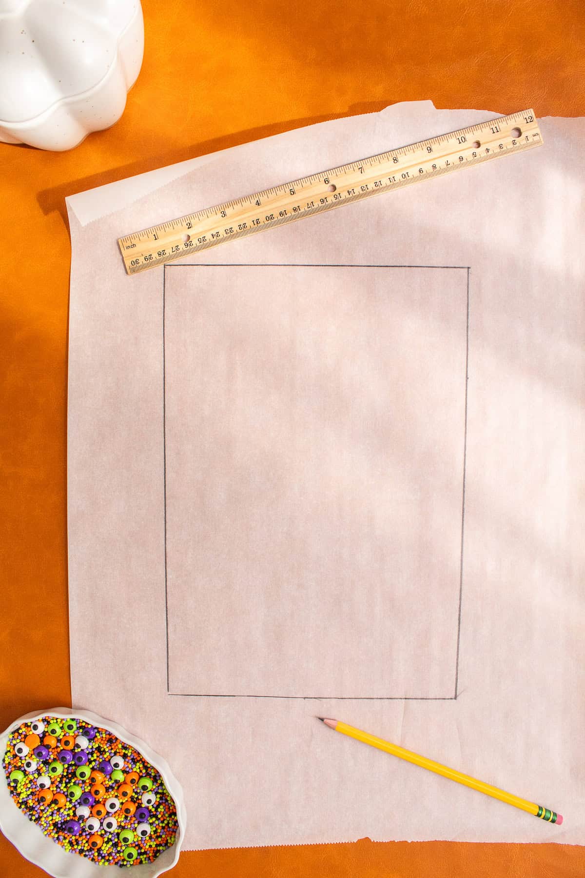 A pencil and ruler are scattered over a large piece of parchment paper with a rectangle traced over it.
