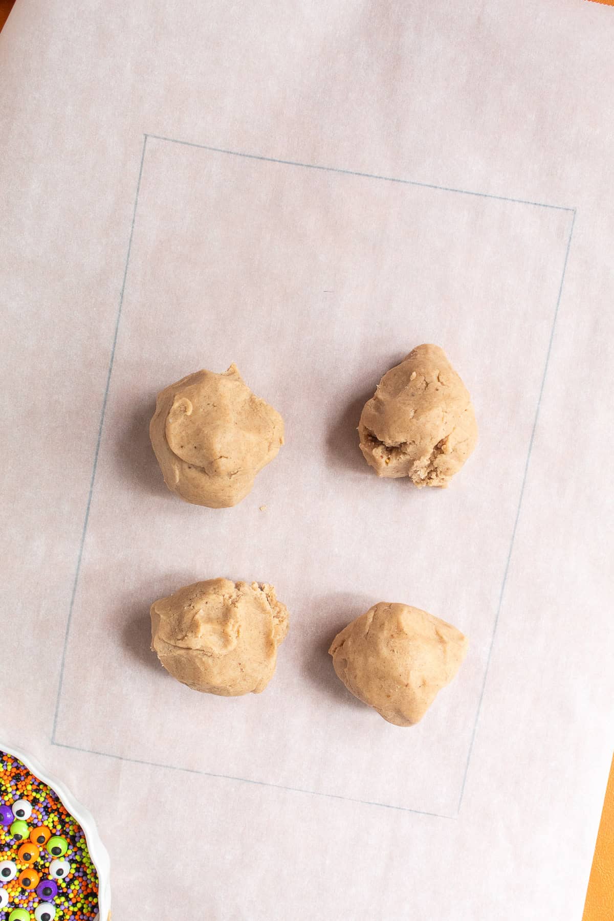 Four balls of spiced shortbread dough sit on a piece of parchment paper.