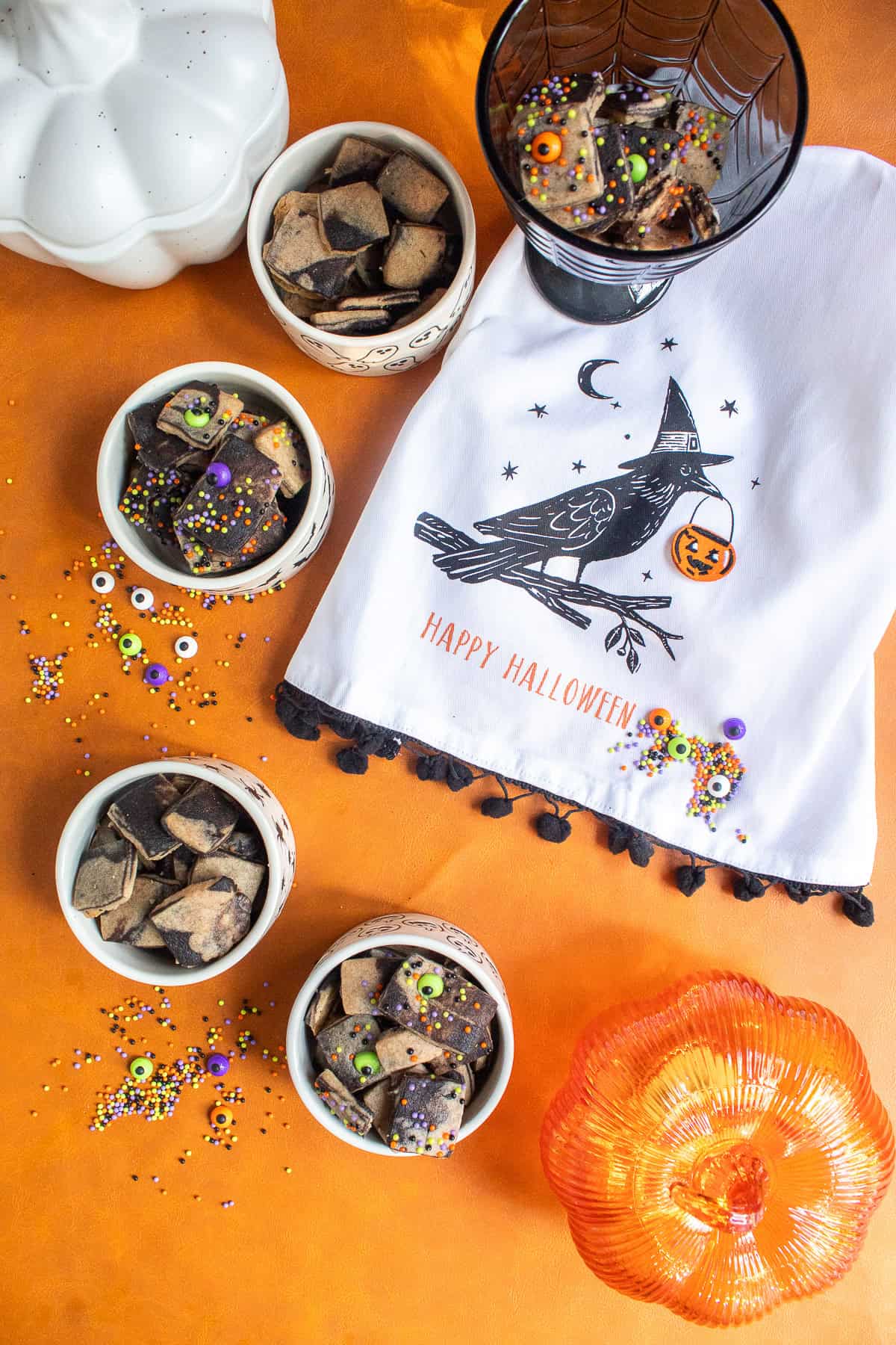 Four small bowls of the baked cookies are scattered over an orange background alongside other Halloween decorations.