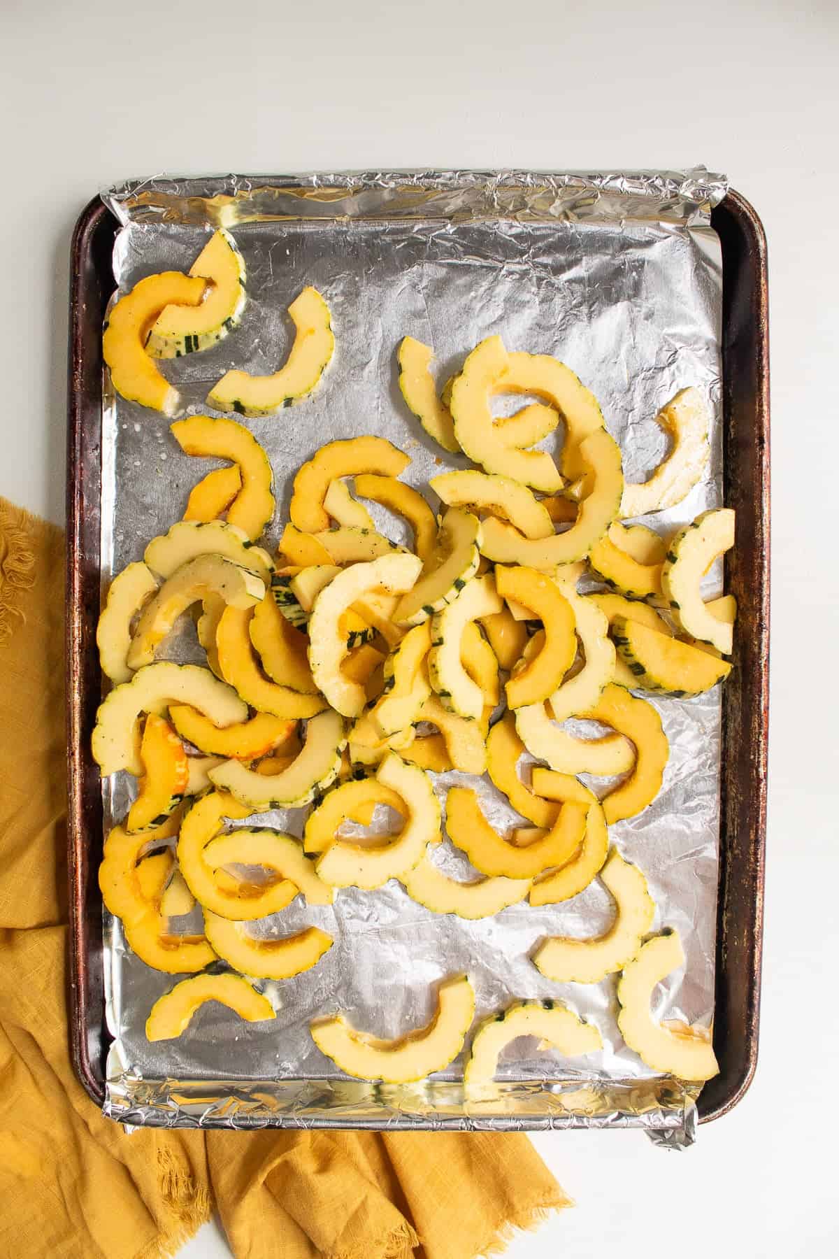 The squash slices are tossed with oil and seasoning on on of the sheet pans.