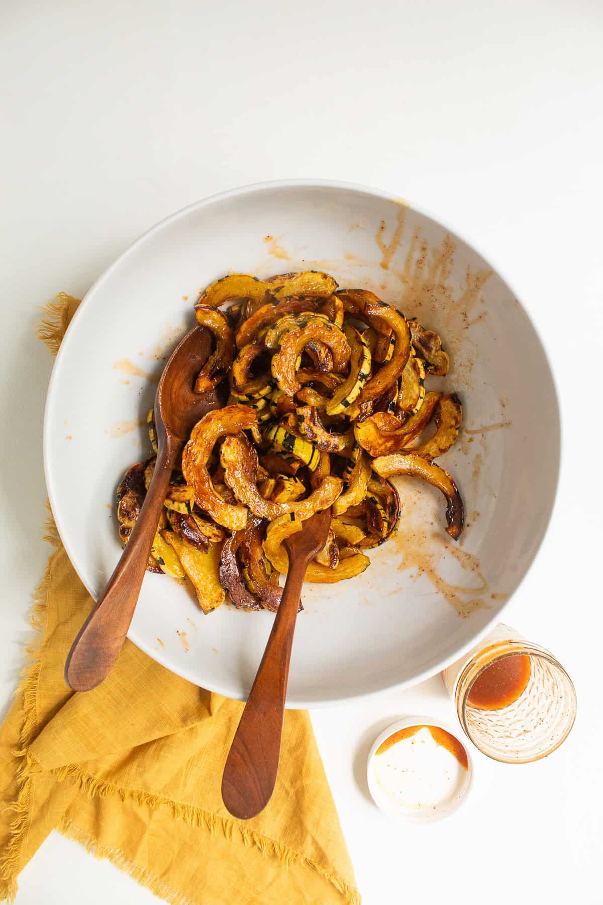Roasted delicata squash slices are tossed with the vinaigrette in a large white bowl.