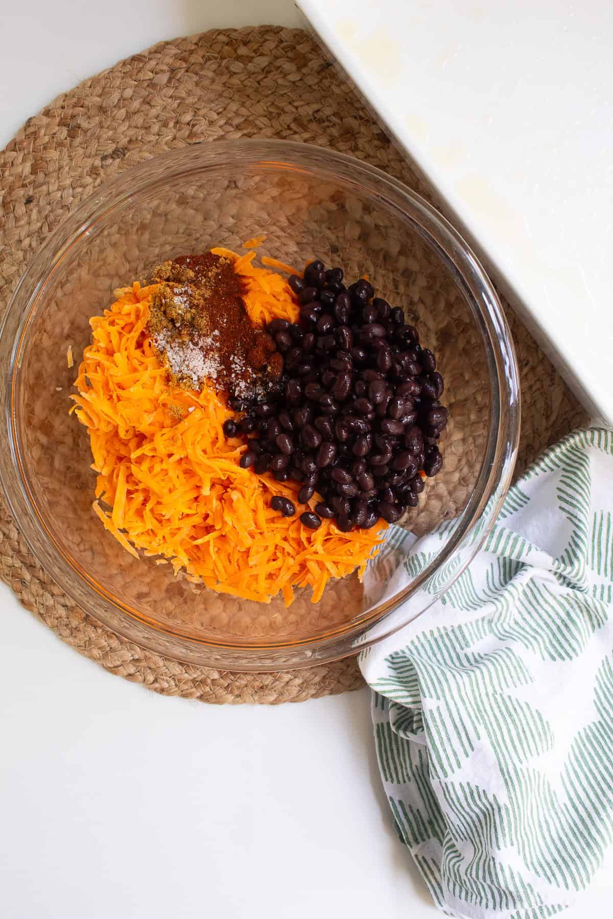 Sweet potato, spices, salt, and beans are added to a glass bowl.