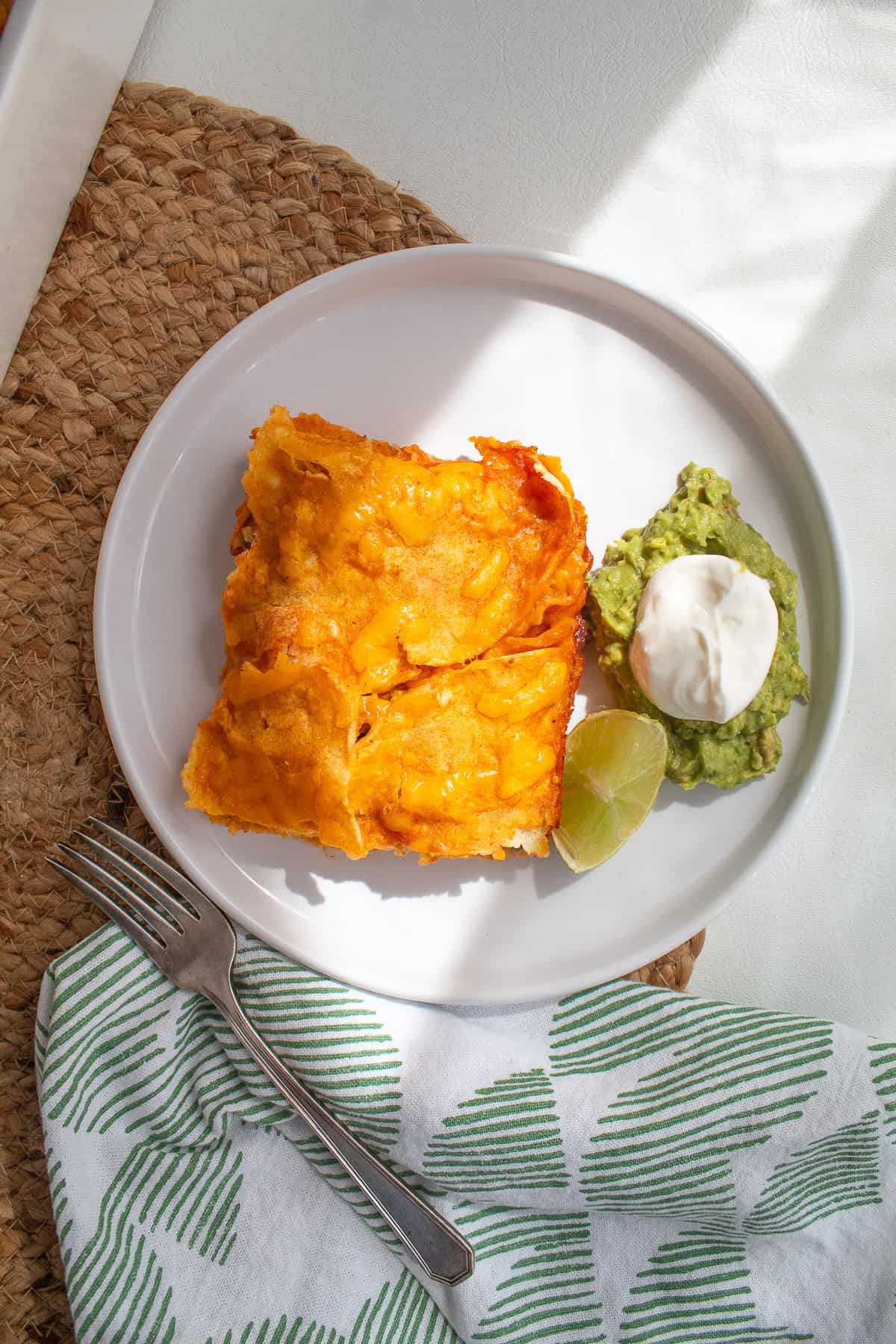 A slice of the enchiladas is garnished with guacamole, sour cream, and a wedge of lime.